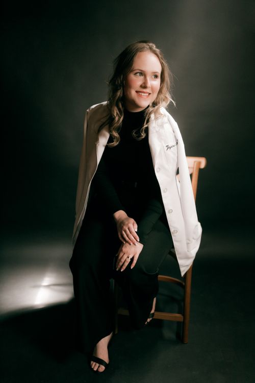 Free A portrait of a smiling female doctor in a studio, seated on a chair, wearing a white coat. Stock Photo