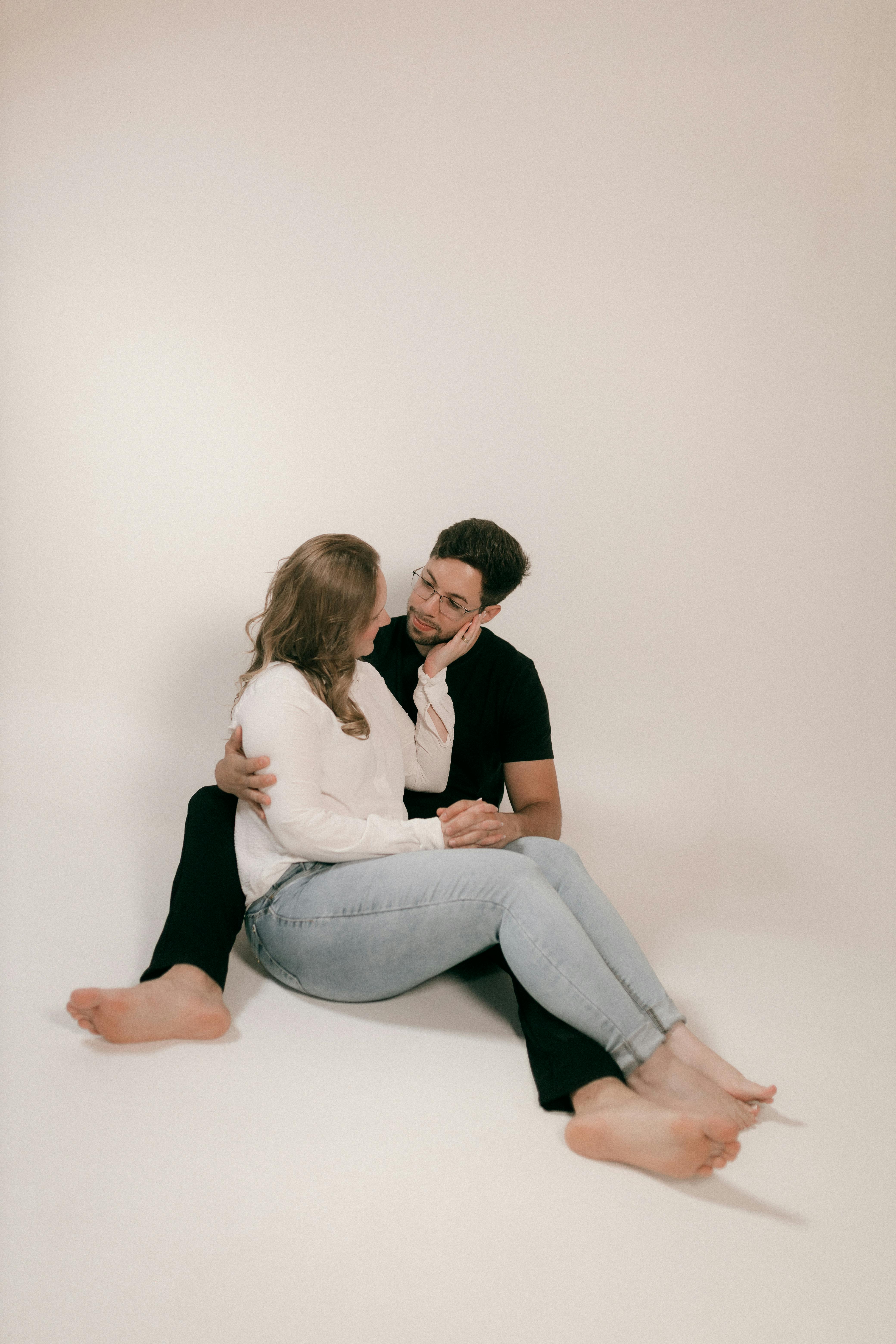 Bezpłatne Szczęśliwa para siedzi na białym tle, obejmuje się i serdecznie uśmiecha. Zdjęcie z galerii