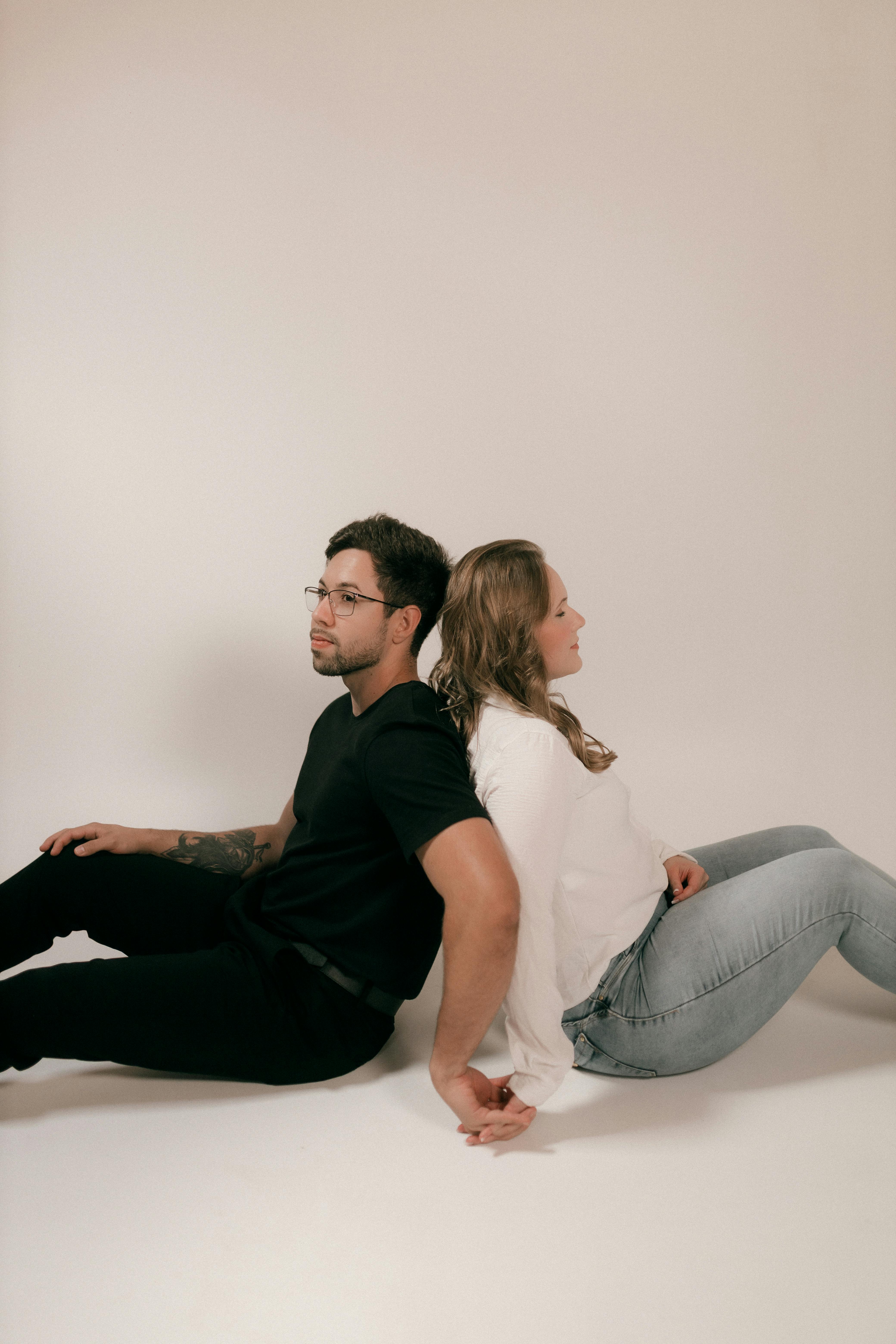 Gratis Una coppia seduta schiena contro schiena si tiene per mano, esprimendo unità e sostegno. Foto a disposizione