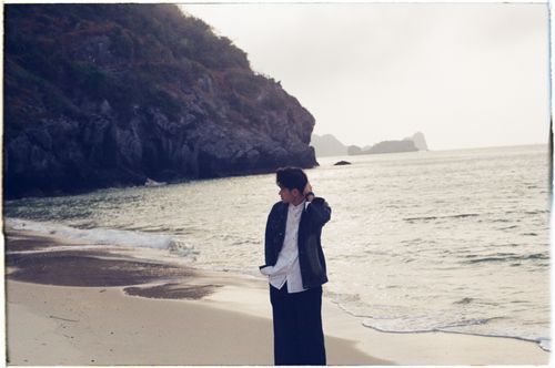 Free A young adult walking on a quiet beach with rocky cliffs, exuding a peaceful morning vibe. Stock Photo