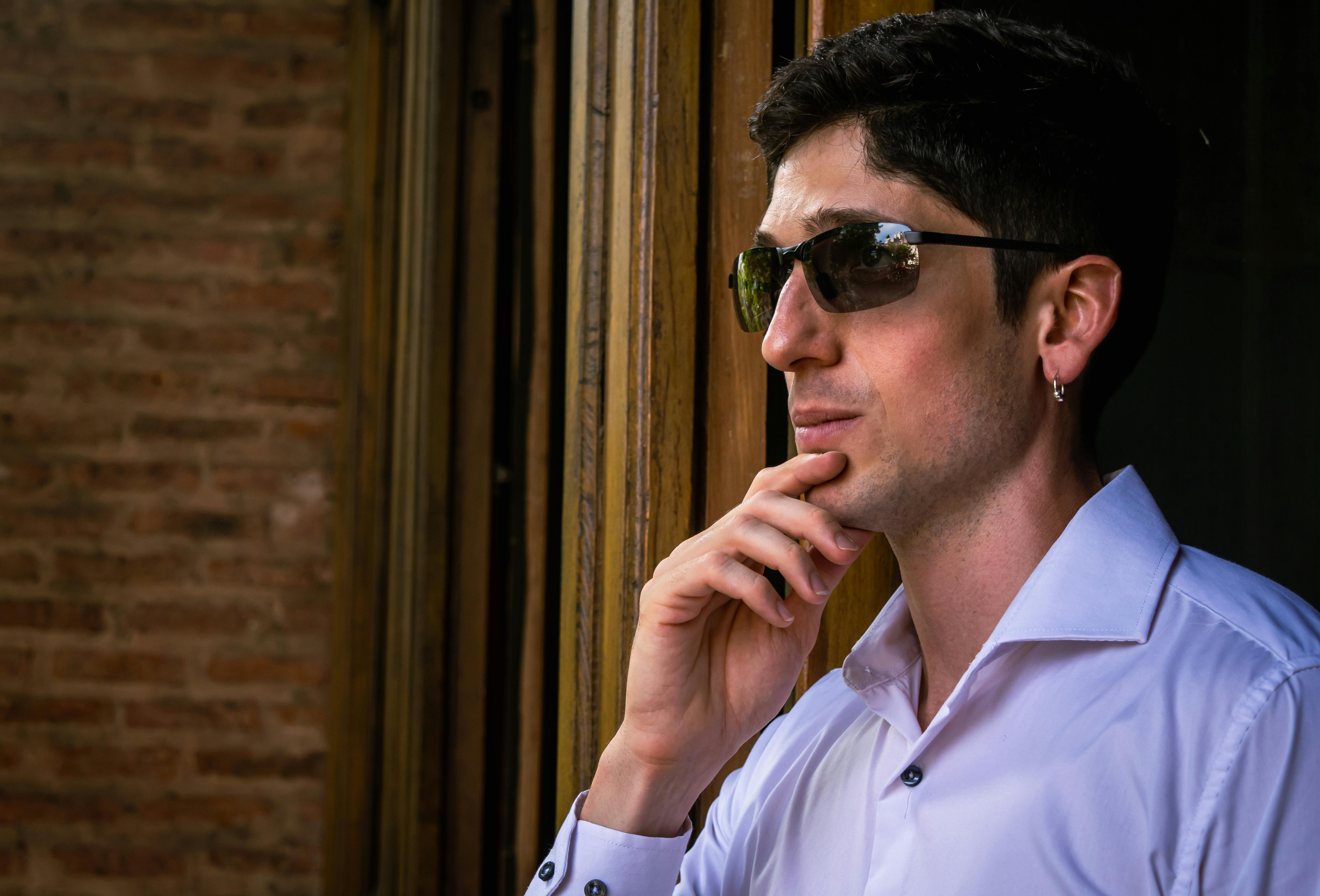 Gratis Profilo di un uomo contemplativo con occhiali da sole che guarda fuori dalla finestra. Foto a disposizione