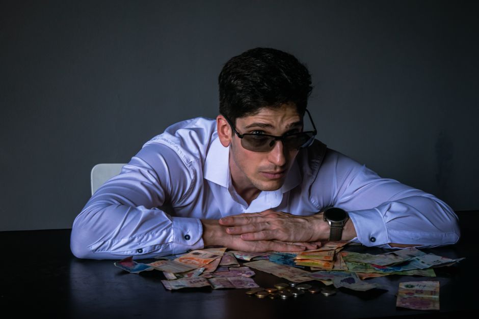 Portrait of a man in sunglasses leaning over a table covered with various currencies. Portrait of a man in sunglasses leaning over a table covered with various currencies.