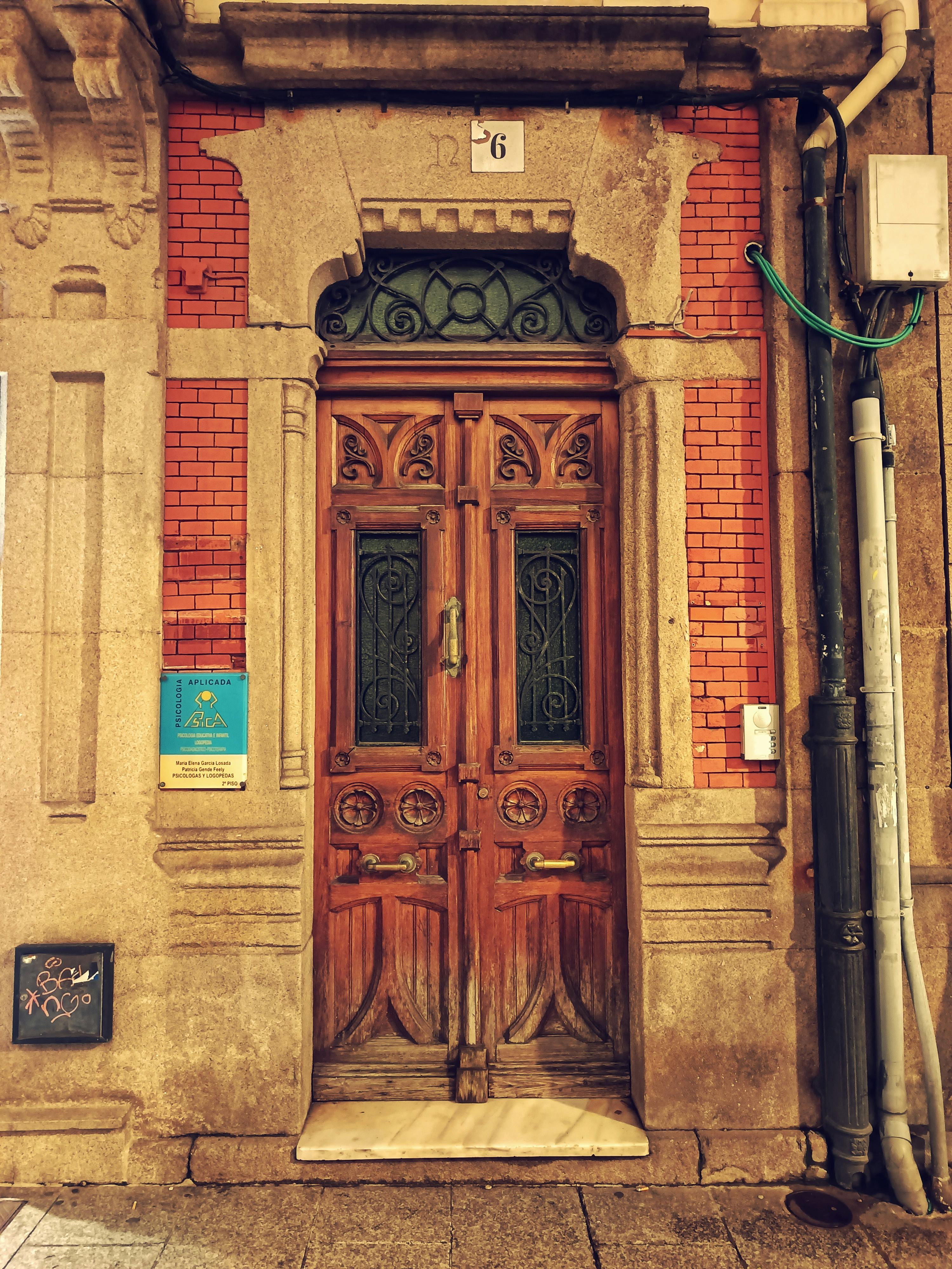 Gratuit O ușă vintage din lemn, cu sculpturi complexe, amplasată într-un zid rustic de cărămidă, prezentând arhitectura europeană clasică. Fotografie de stoc