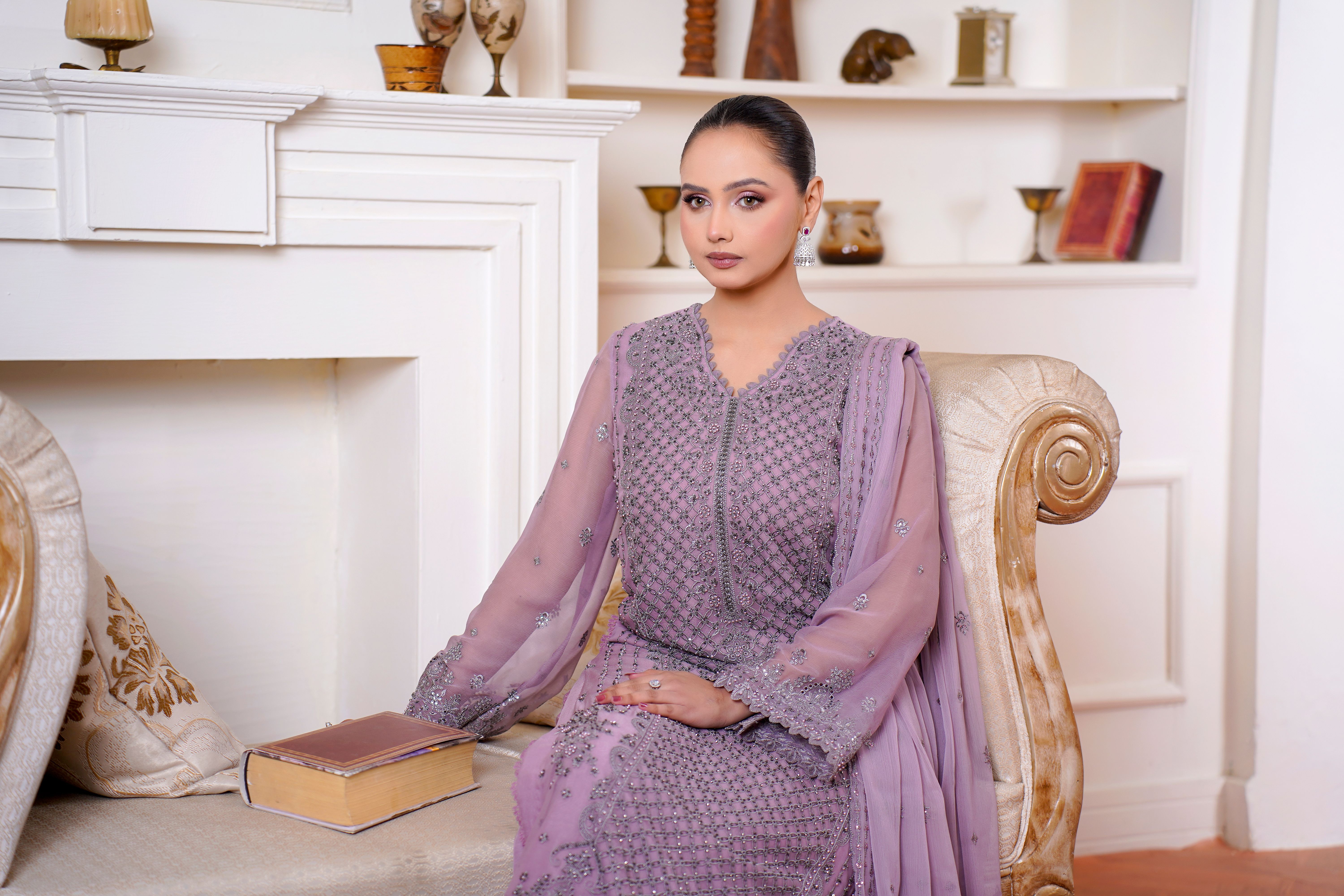 Woman in lavender embroidered dress seated elegantly in a sophisticated setting.