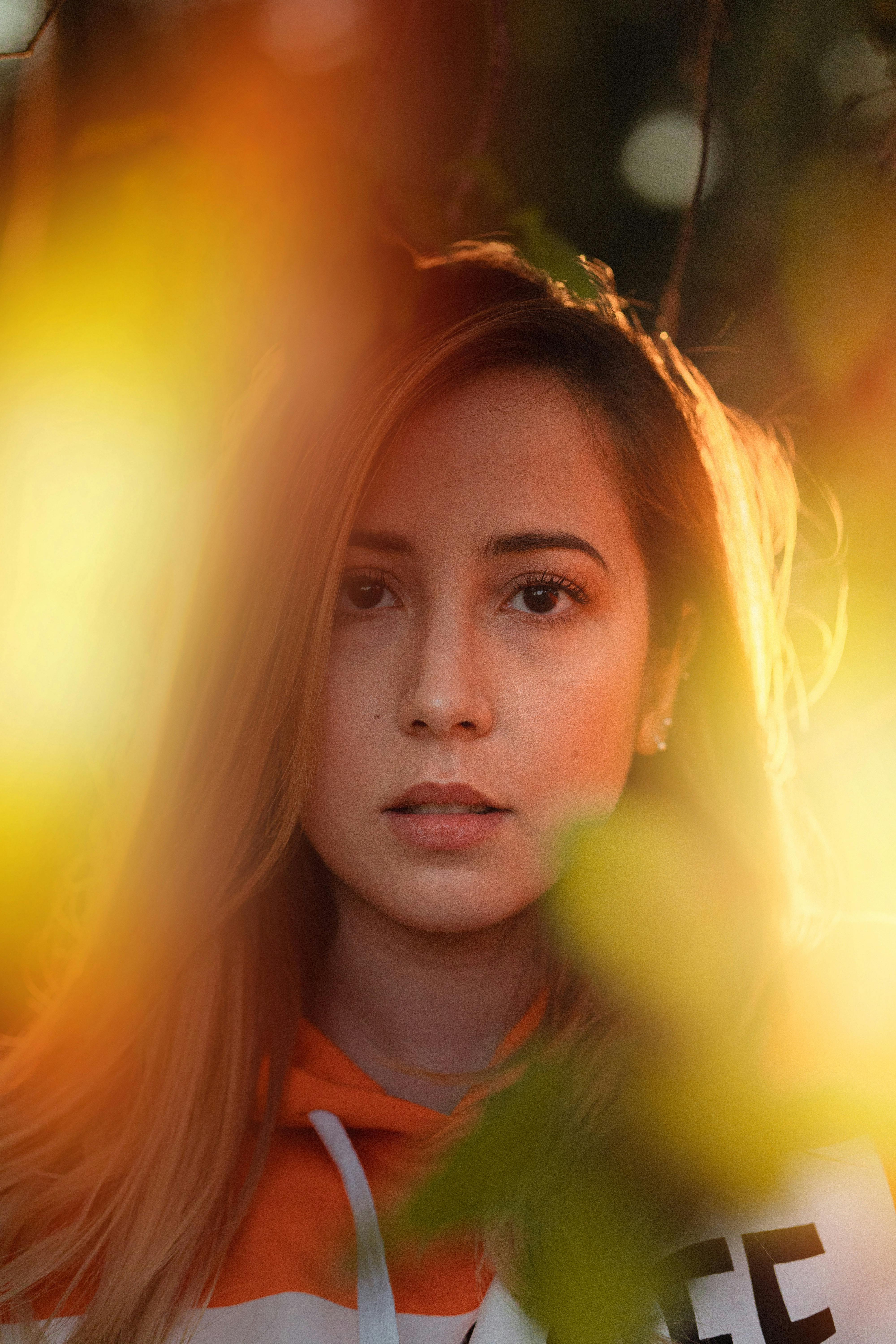 Warm-toned portrait of a woman amidst nature, featuring soft light and blurred foliage.