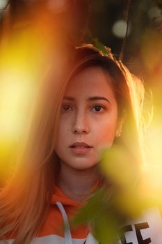 Warm-toned portrait of a woman amidst nature, featuring soft light and blurred foliage.