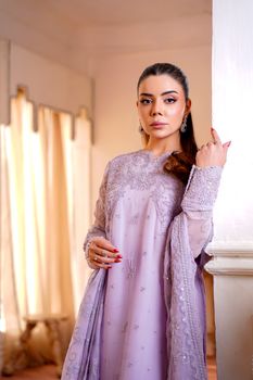 A sophisticated woman poses in an embroidered lavender dress indoors.