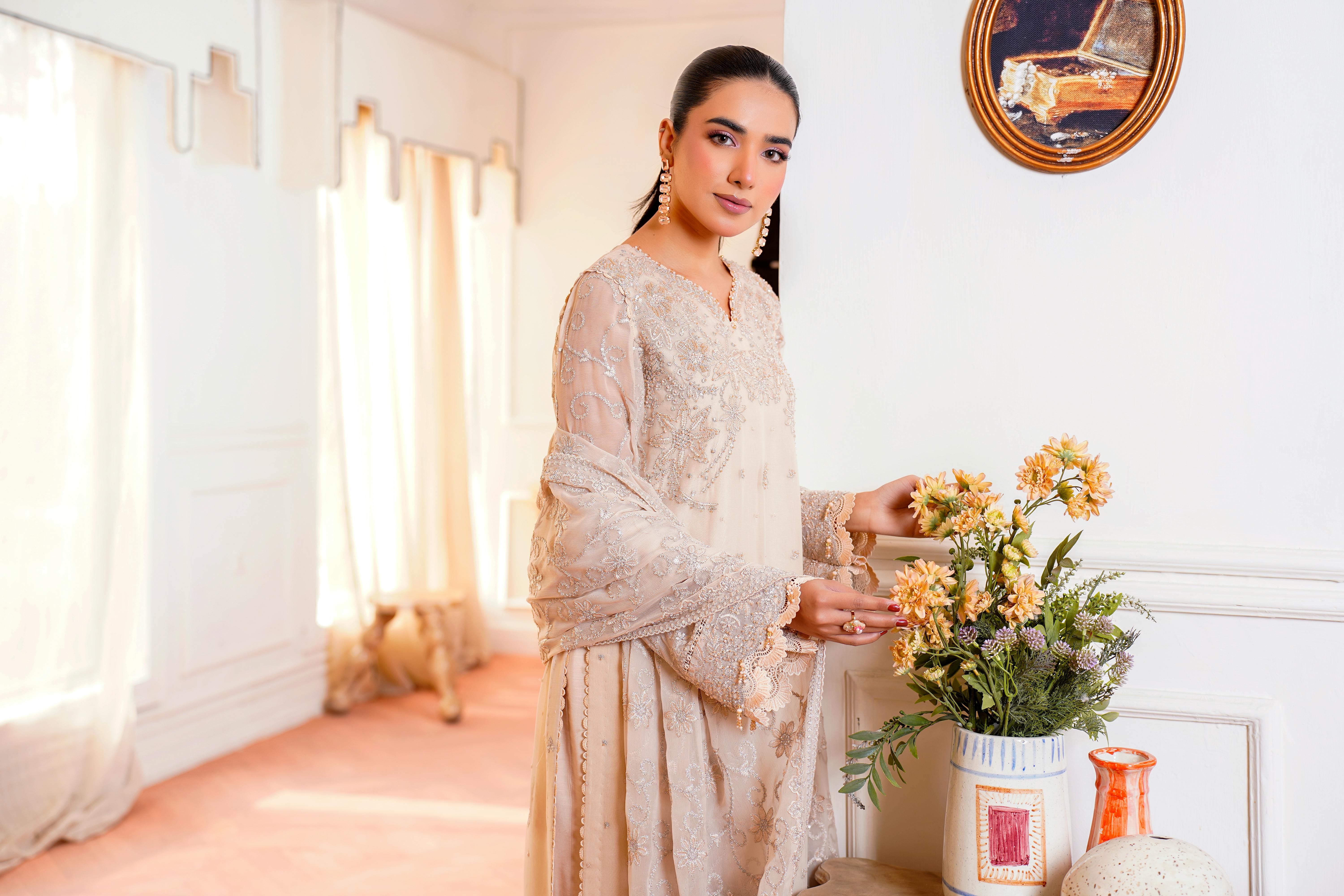 gratis Een elegante vrouw poseert binnenshuis in een prachtige geborduurde jurk naast een bloemstuk. Stockfoto