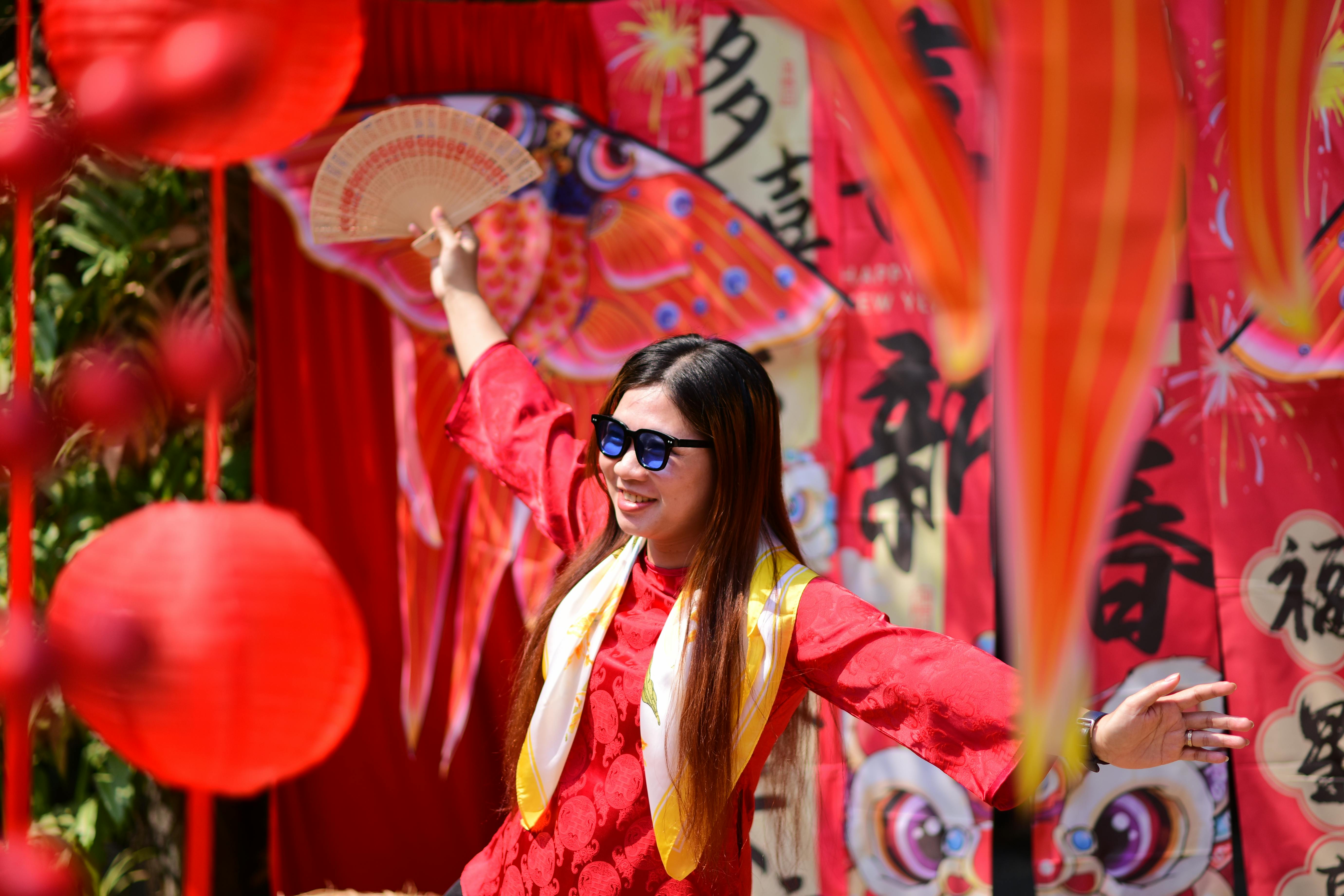 A woman joyfully celebrating Chinese New Year outdoors with red decorations and traditional attire.