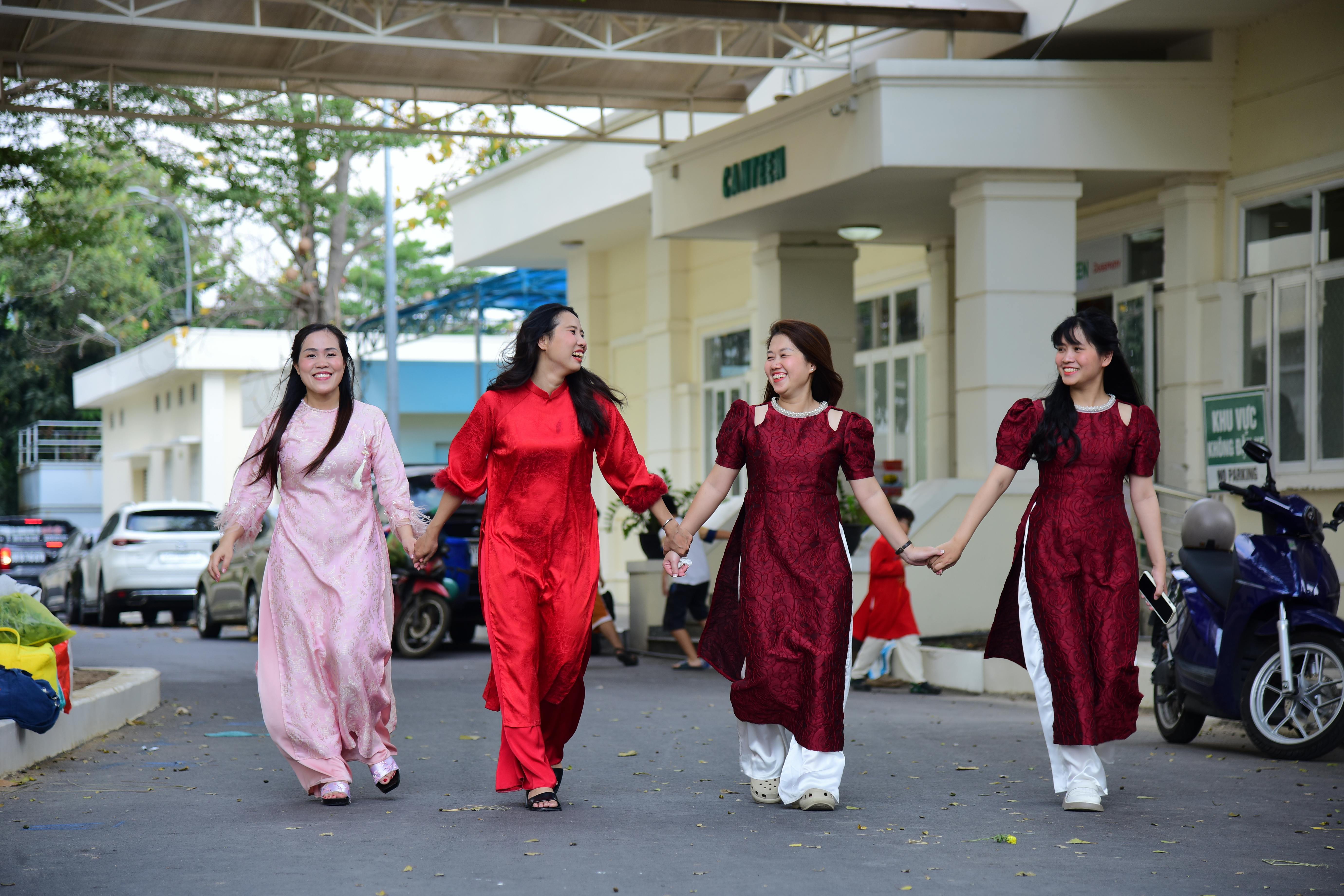 Free Four women in vibrant ao dai dresses walking together, smiling and holding hands outdoors. Stock Photo