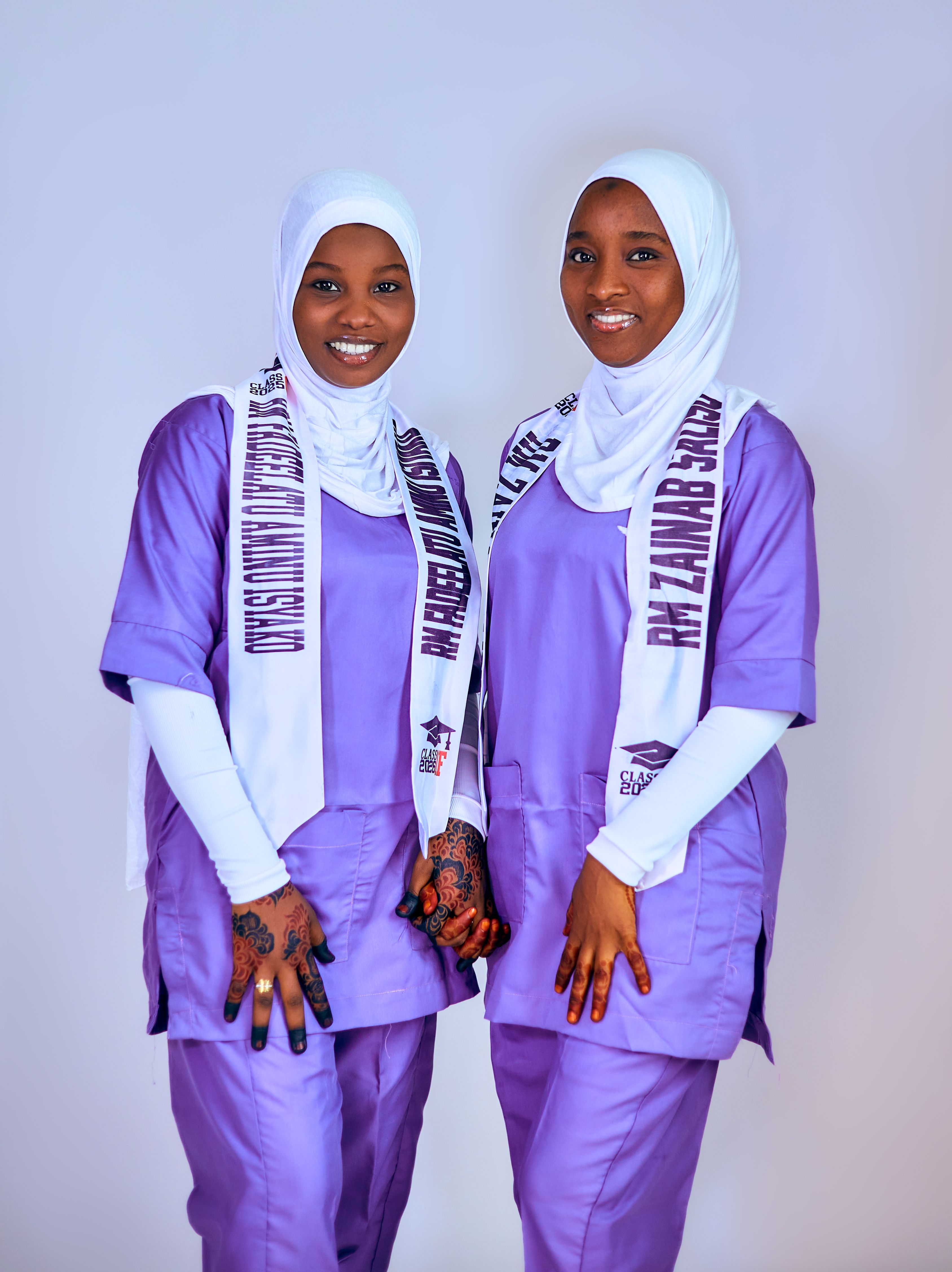 Two smiling women in purple attire and custom white scarves posing confidently indoors.