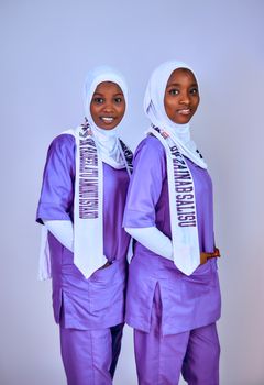 Two women wearing purple traditional attire with white hijabs pose against a plain background. - Fotografer Sidoarjo