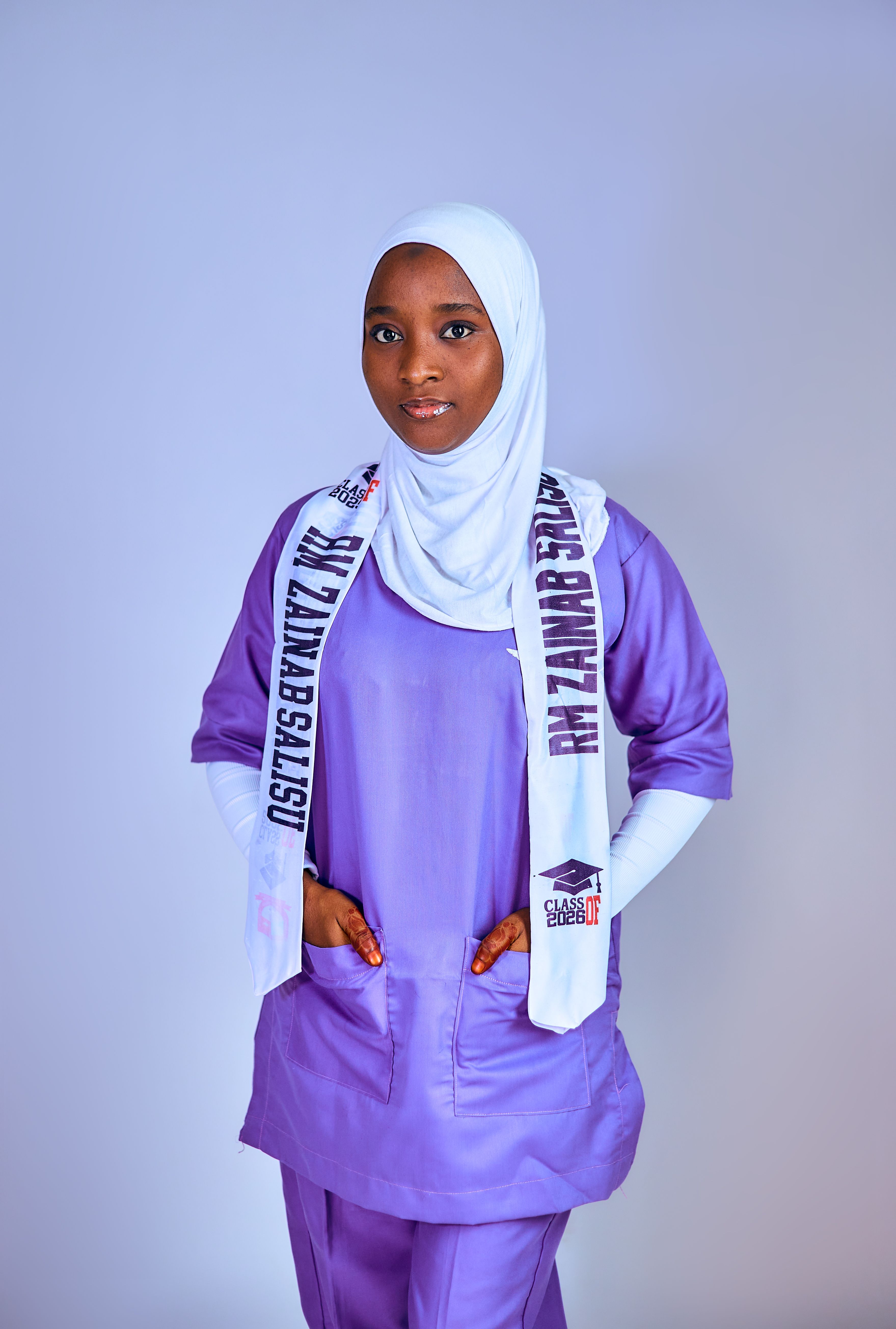 Young woman wearing purple medical attire and a white hijab, standing confidently.