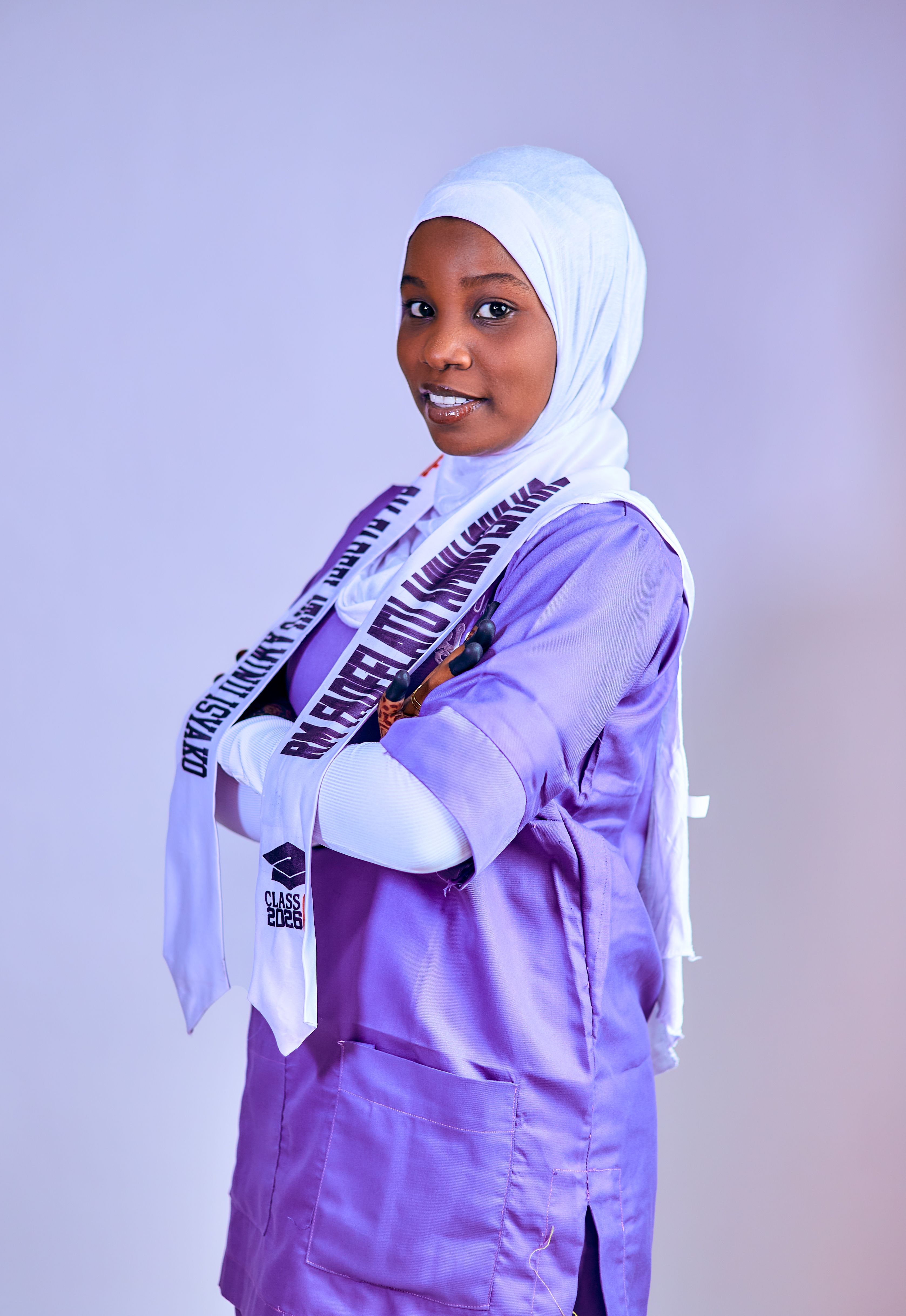 Young female medical professional in purple uniform with arms crossed and confident smile.