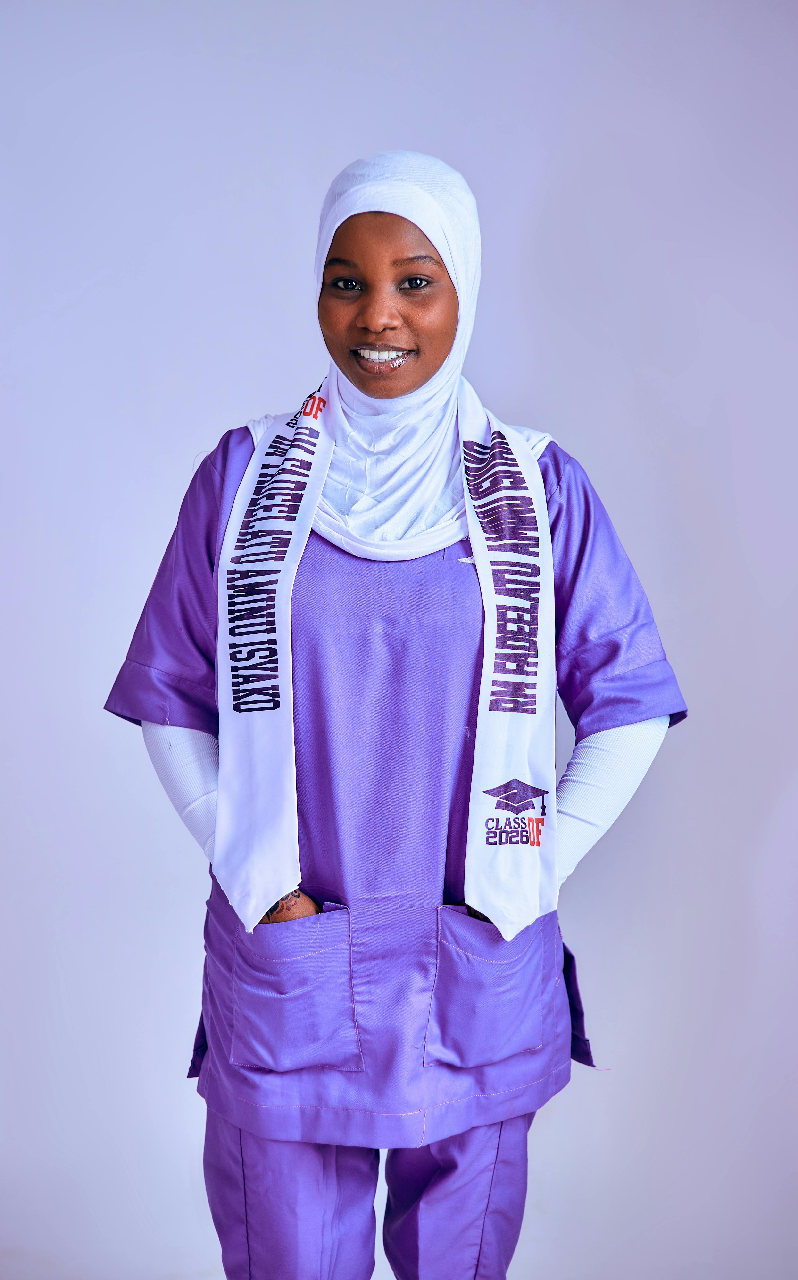 Smiling healthcare professional in a purple uniform with white hijab and graduation stole.