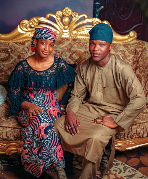 Free A stylish African couple in colorful traditional attire posing on an ornate gold sofa with a patterned backdrop. Stock Photo