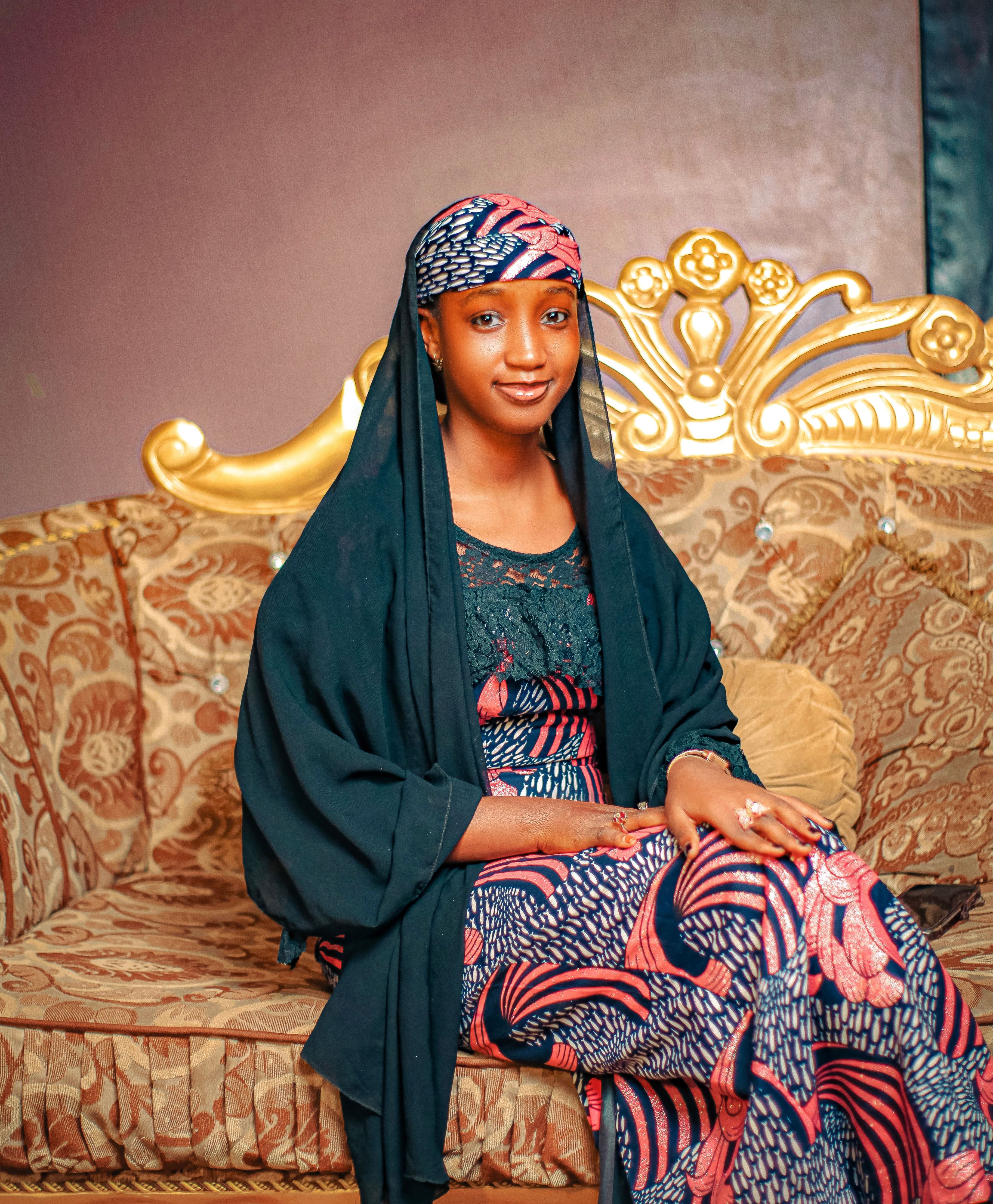 A woman dressed in vibrant traditional clothing is seated gracefully on an ornate sofa indoors.