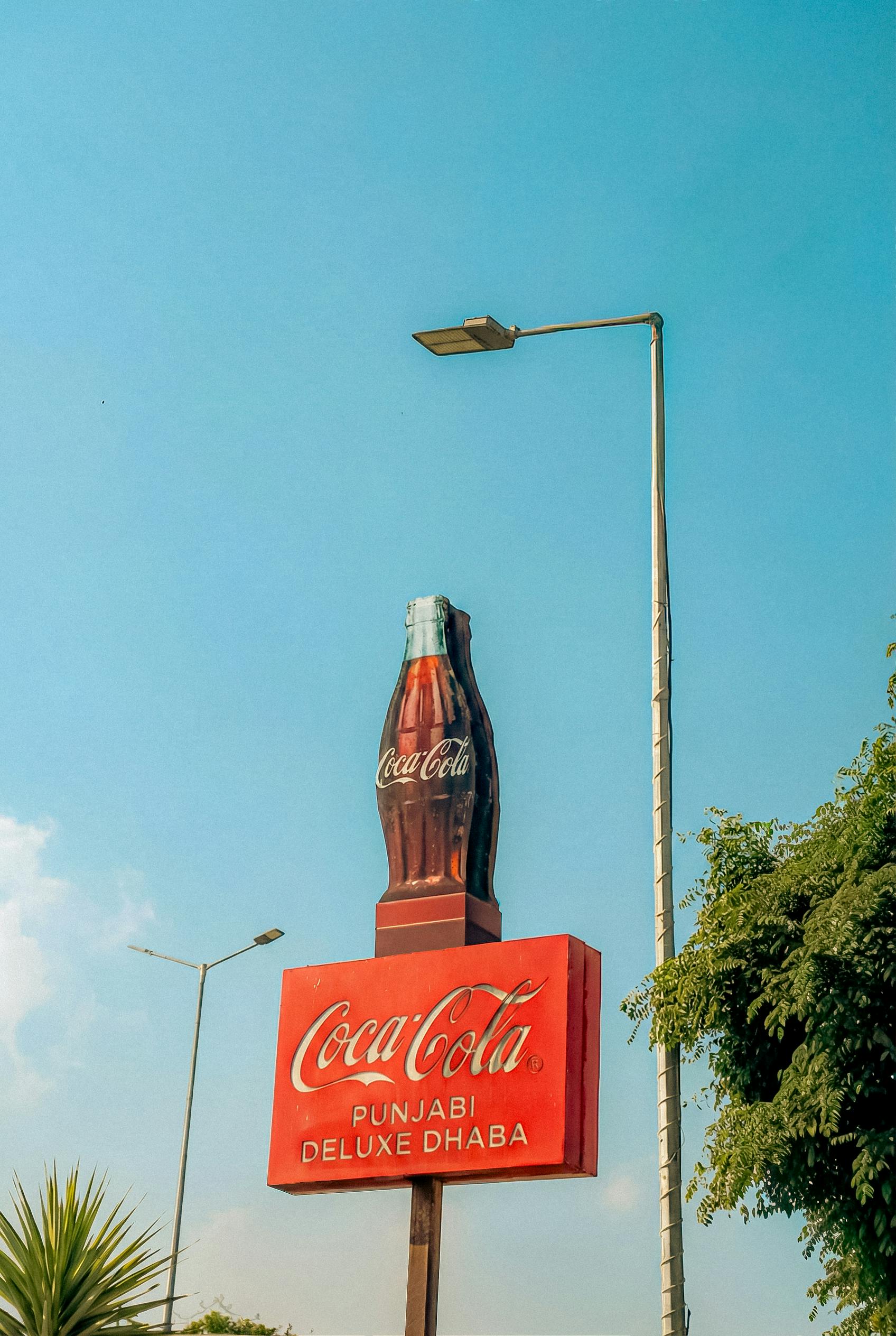 Gratis Papan nama Coca-Cola untuk Punjabi Deluxe Dhaba dengan latar langit biru cerah. Foto Stok