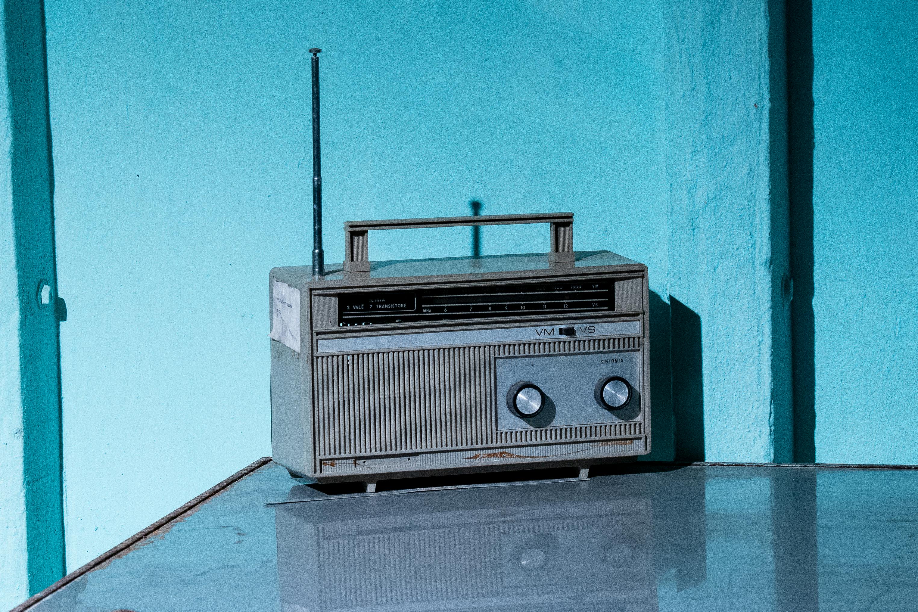 Vintage transistor radio on reflective surface with teal background, casting shadows.