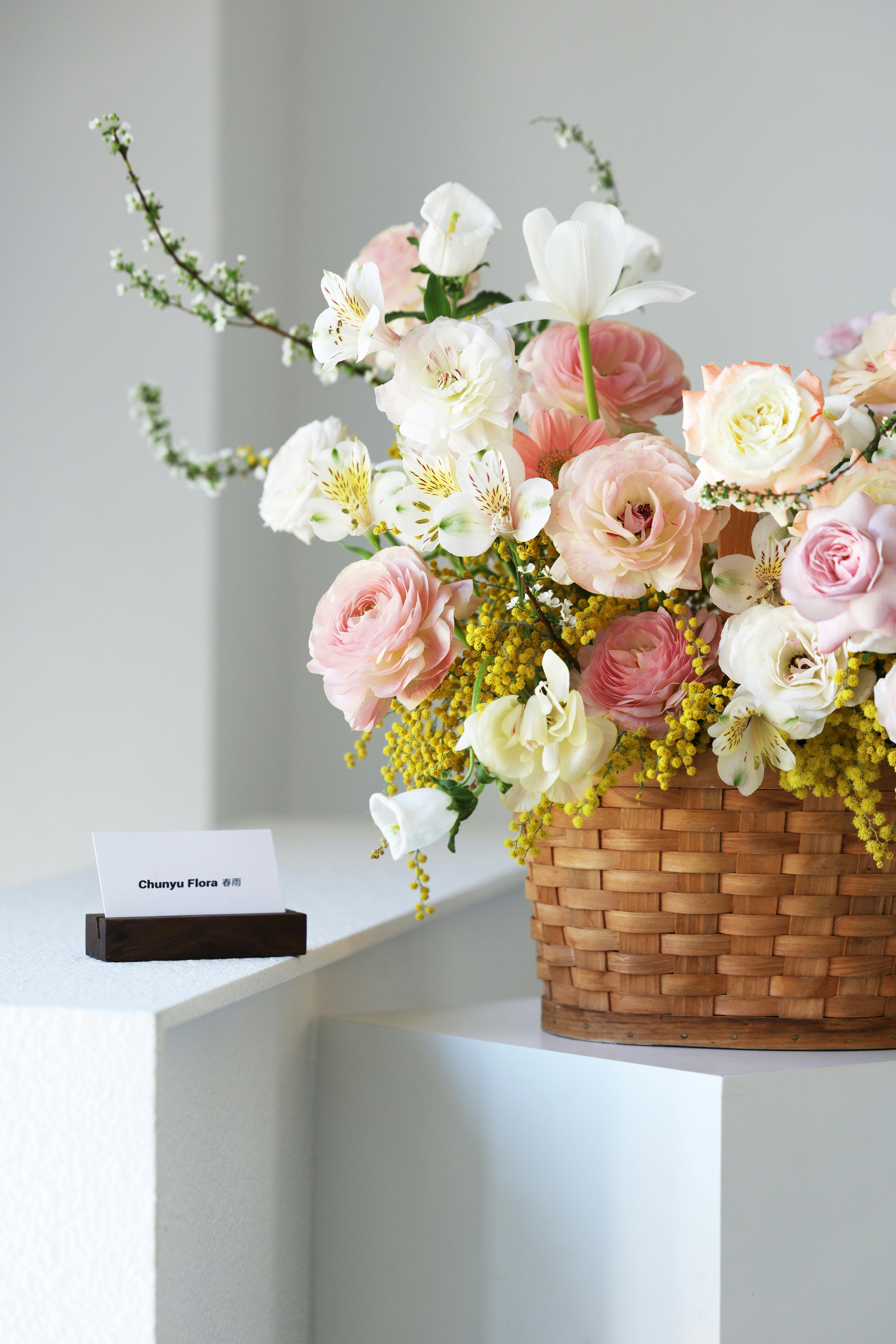 Δωρεάν Όμορφη ανθοδέσμη με ανάμεικτα λουλούδια σε ένα καλάθι σε ένα λευκό βάθρο σε εσωτερικό χώρο, που αποτυπώνει τη λεπτή λουλουδάτη ομορφιά. Φωτογραφία από στοκ φωτογραφιών