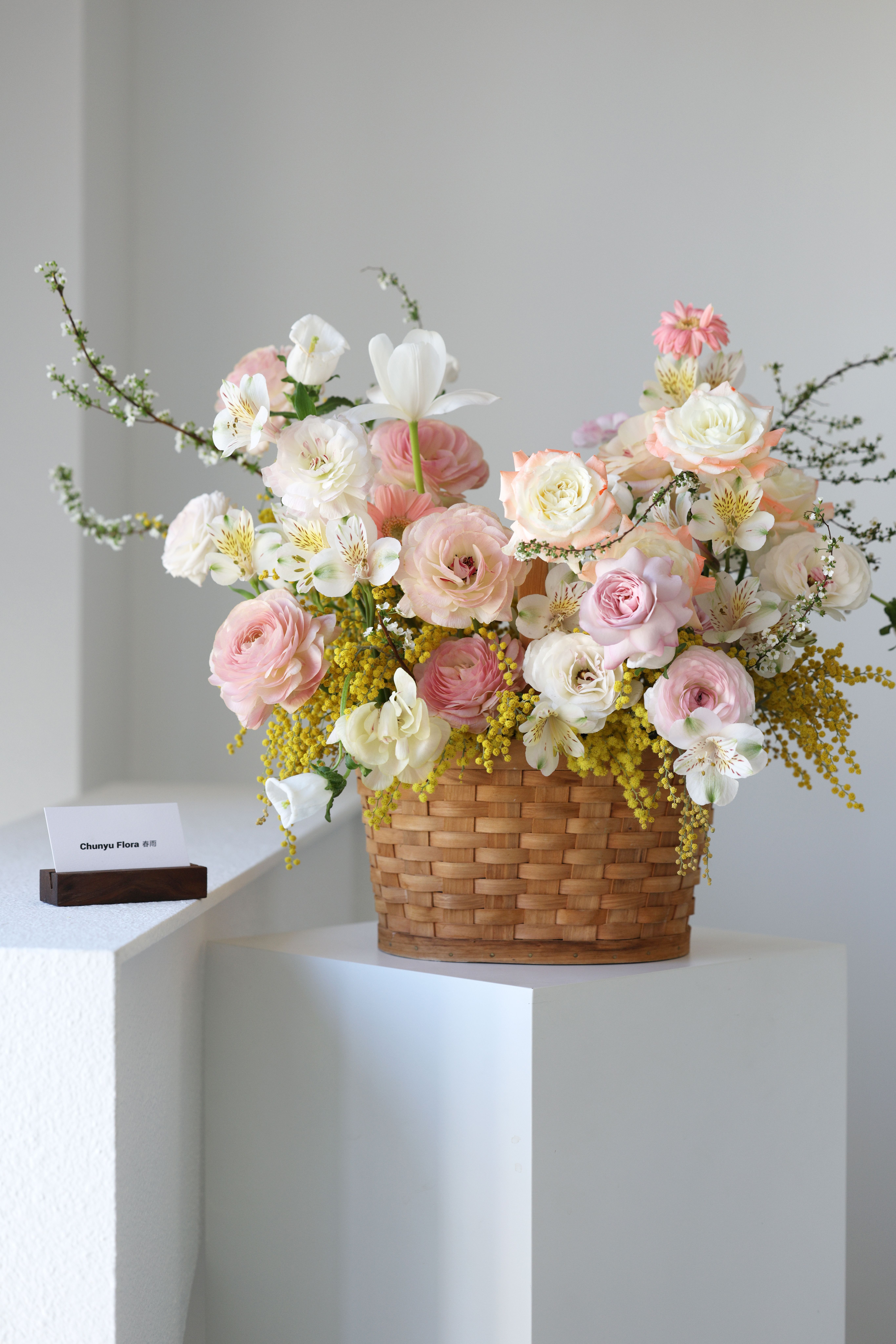 A beautiful arrangement of pastel flowers in a basket on a white pedestal indoors. - Fotografer Sidoarjo