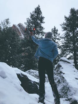 Person flying a drone in a snowy mountain landscape, capturing winter's serene beauty.
