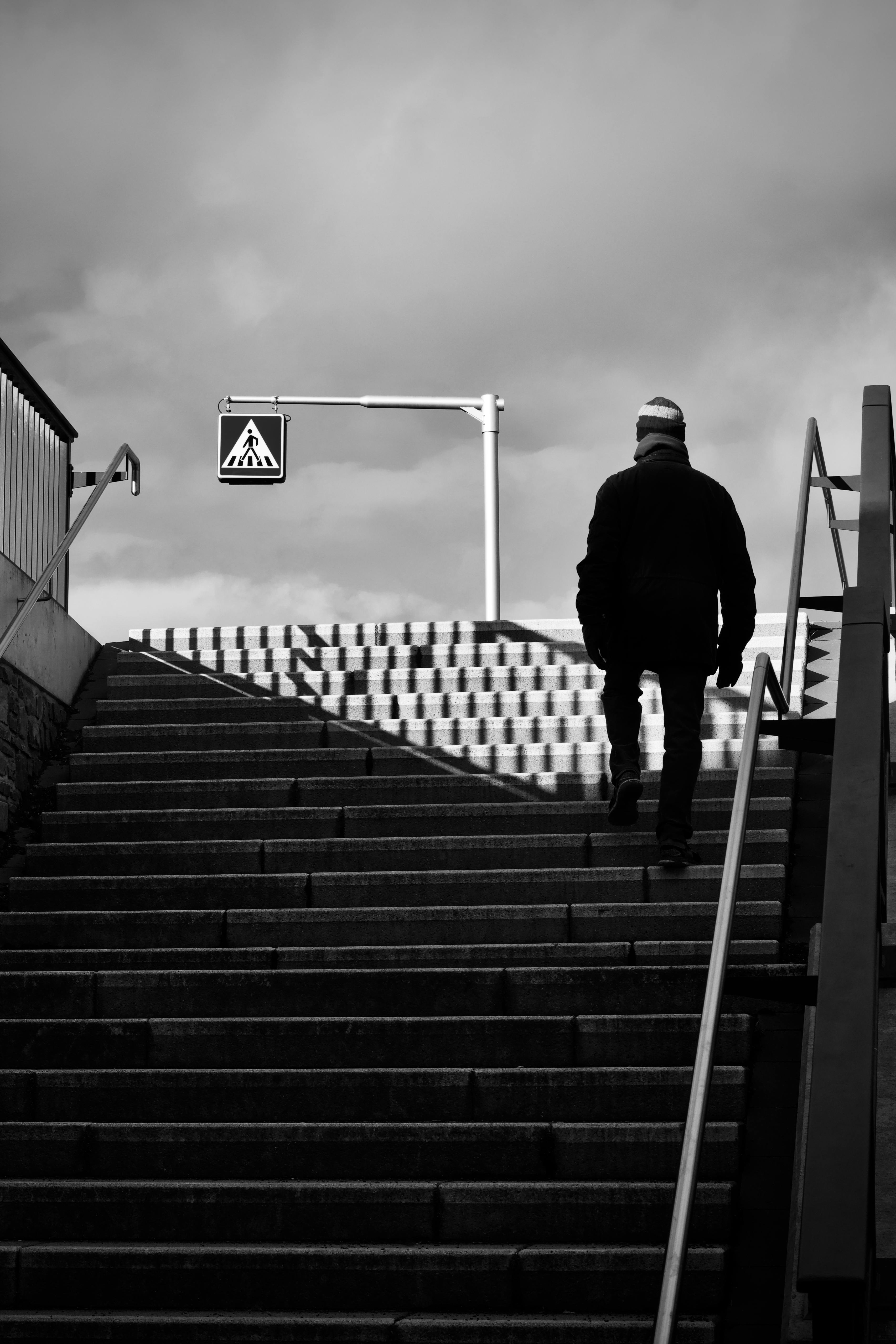 Gratuit Image en noir et blanc d'un homme en tenue d'hiver montant un escalier avec un panneau au-dessus de lui. Photos