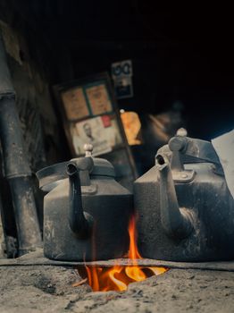 Two vintage metal kettles on a rustic fire stove. Warm, cozy ambience with orange flames.