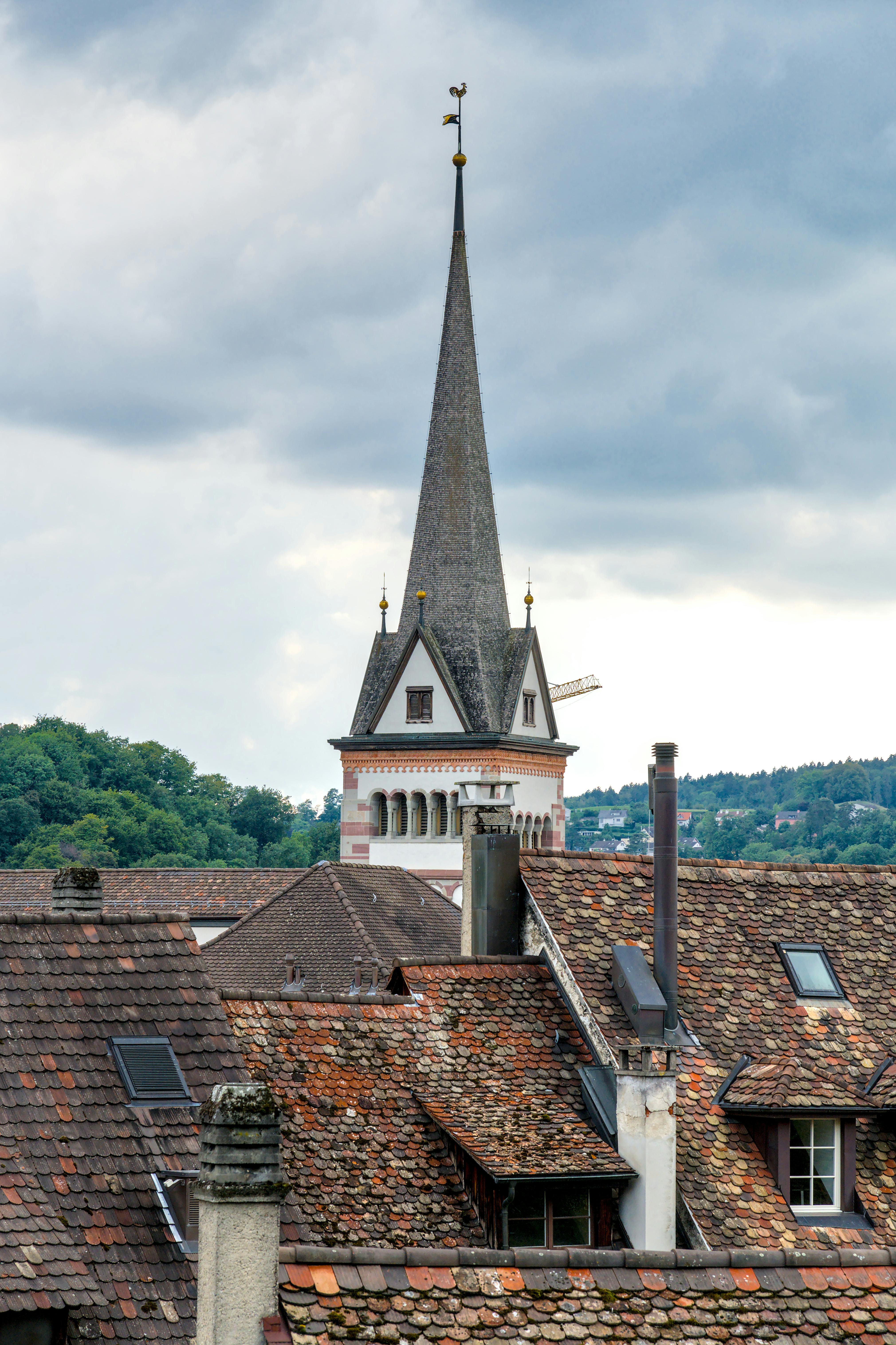 gratis Rustieke daken en een historische kerktoren onder een bewolkte hemel in een Zwitsers stadje. Stockfoto