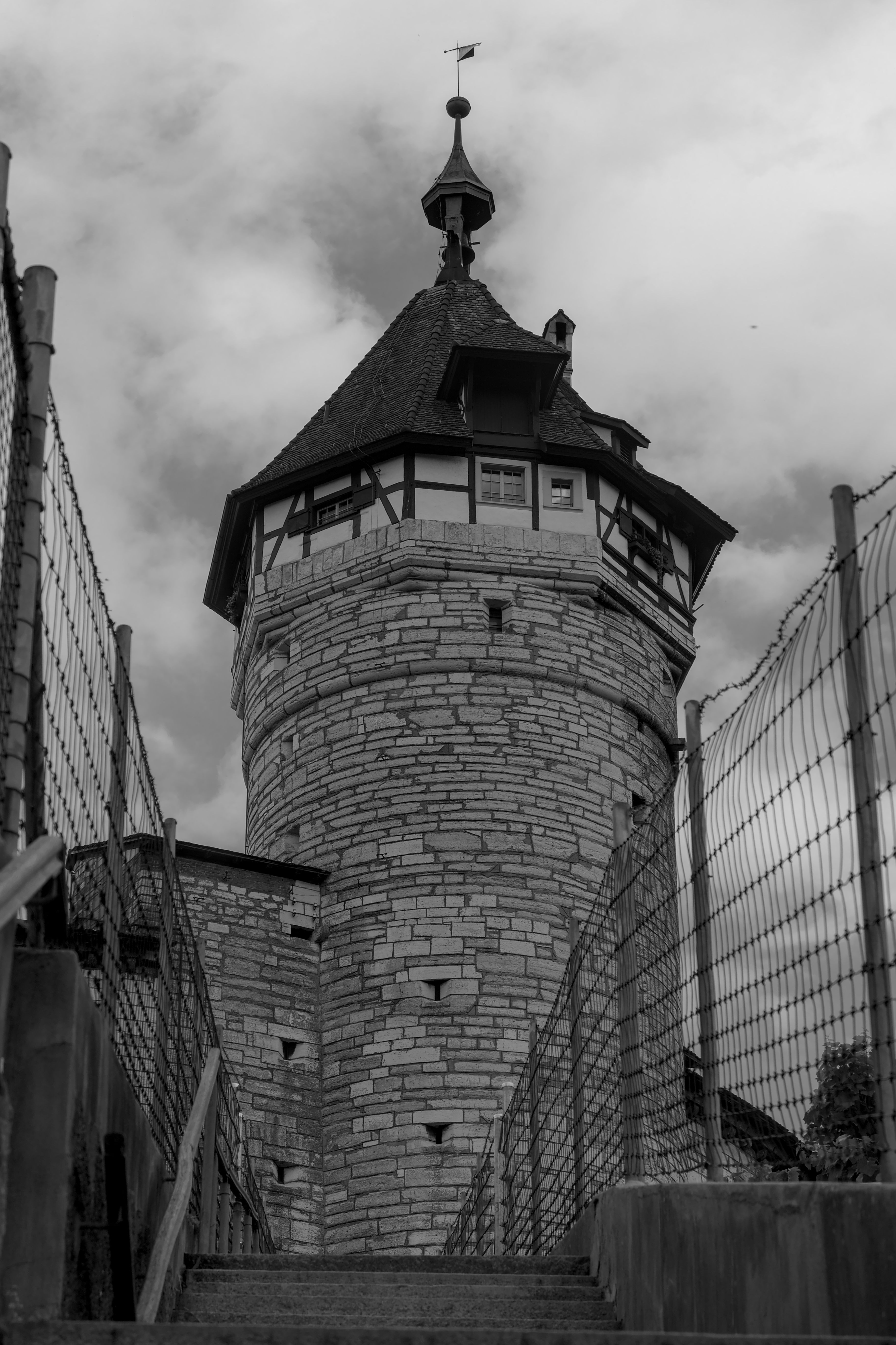 A striking black and white photo of a historic stone tower with a wooden roof against a cloudy sky.