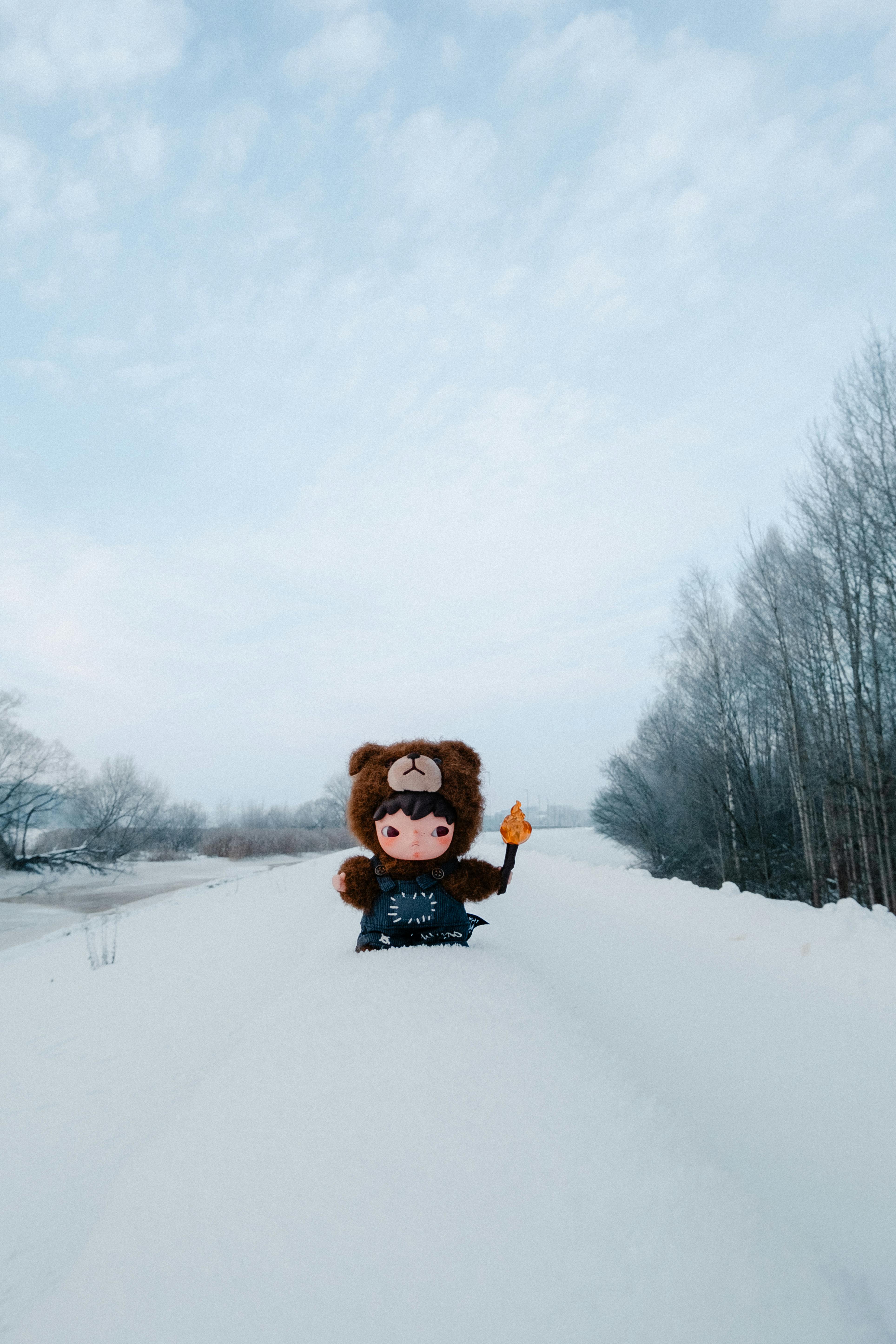 Безкоштовне Химерна фігурка ведмедя в костюмі ведмедя, що тримає іграшку, розташована на тлі безтурботної засніженої зимової сцени. стокове фото