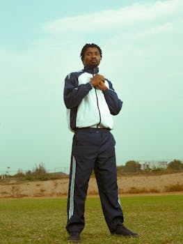 A young man in athletic wear stands confidently in an open field under a bright sky.