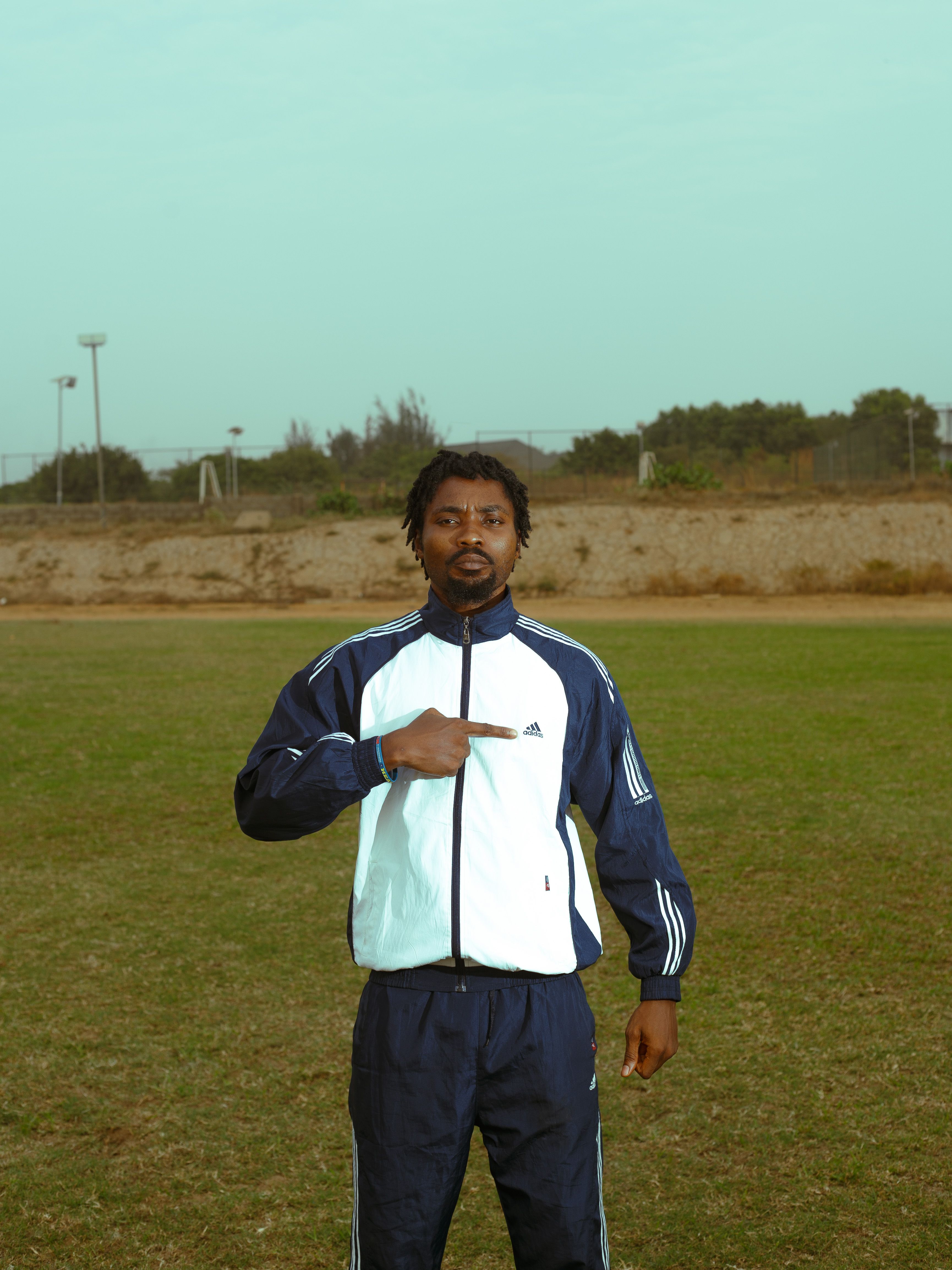 Athletic man in a track suit pointing outdoors on a field, showcasing a sporty vibe.