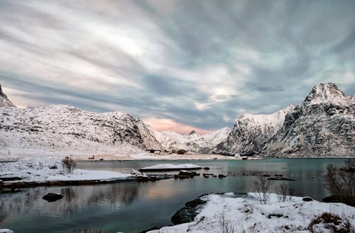 Free Snow Covered Mountain Near Lake Under Cloudy Sky Stock Photo