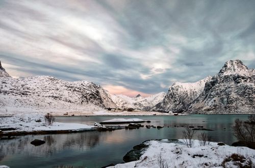 Free Scenic winter view of Flakstad, Norway with snow-covered mountains, fjord, and dramatic sky. Stock Photo