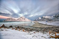 挪威弗拉克斯塔德海滩的冬季景色迷人，白雪皑皑的山脉与戏剧性的天空交相辉映