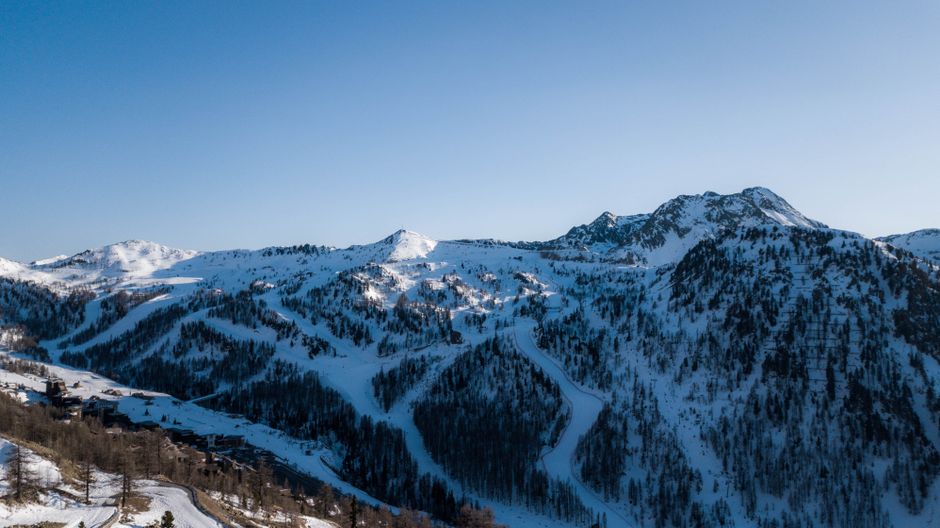 Scenic aerial shot of the snow-covered French Alps during winter, showcasing ski slopes and rugged terrain.