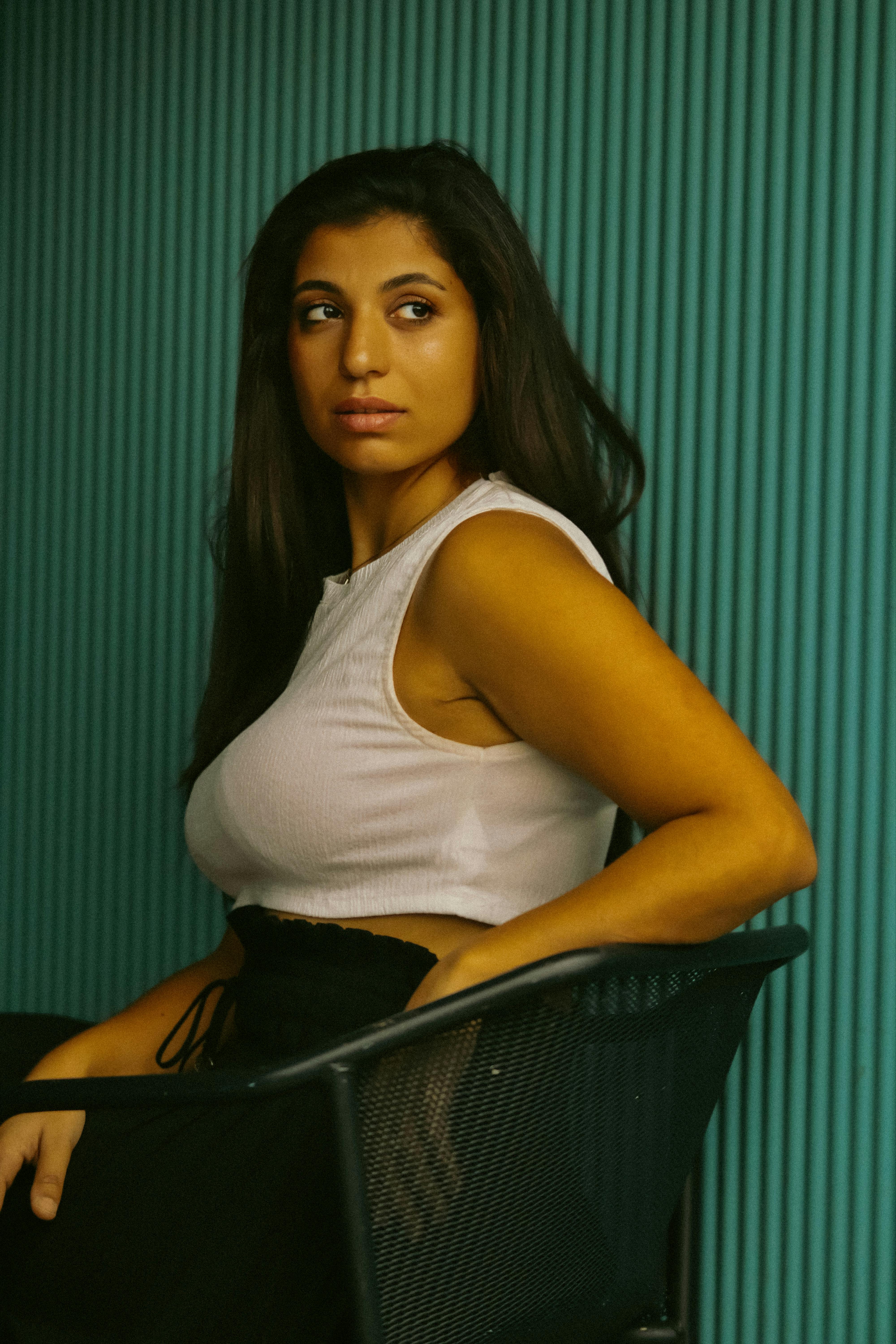 bezplatná Zamyšlená žena s dlouhými vlasy sedí bokem na židli na tyrkysovém pozadí. Základová fotografie