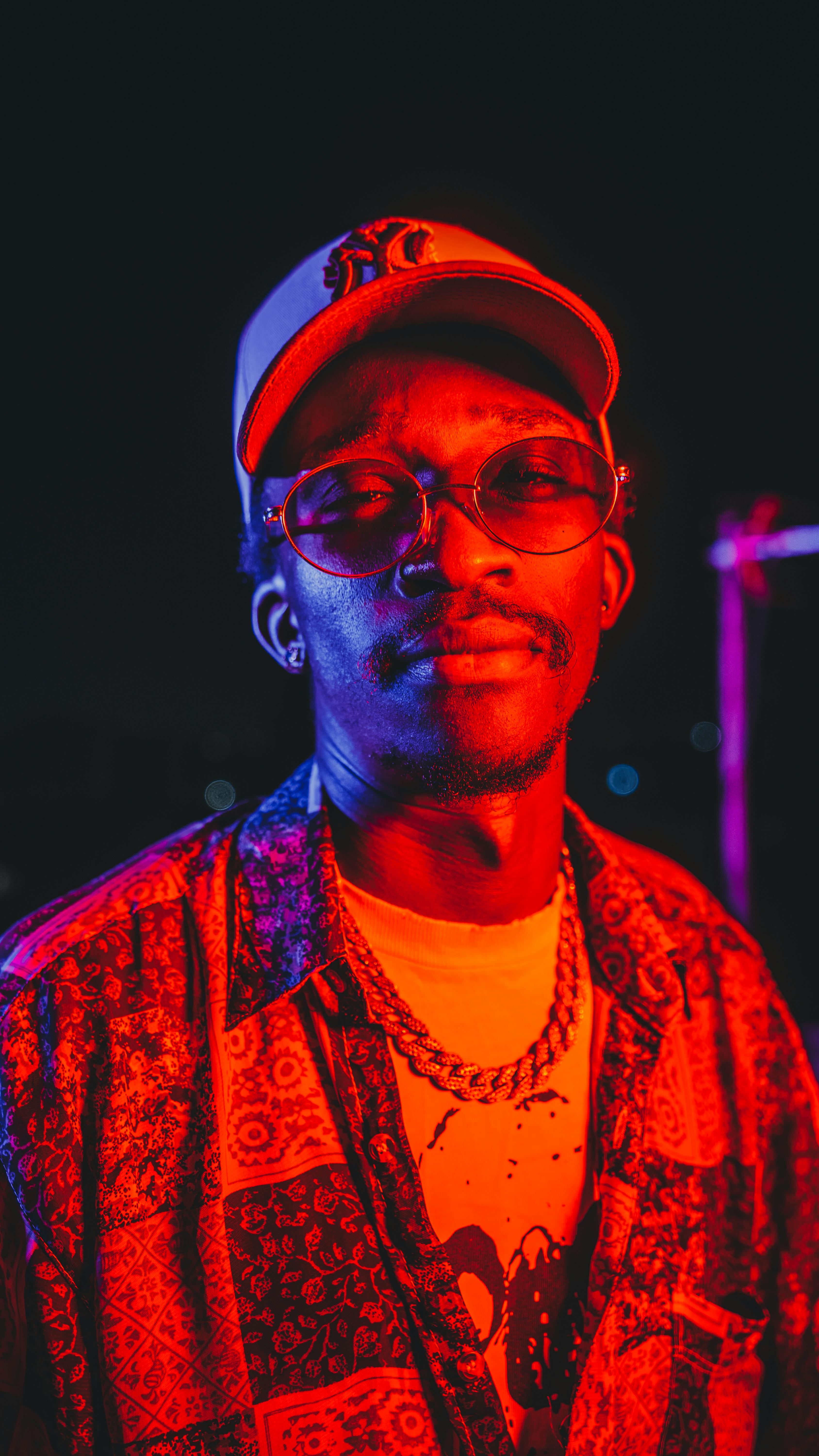 ingyenes Portré egy divatos férfiról merész piros és kék megvilágításban, mintás ingben és sapkában. Stockfotó