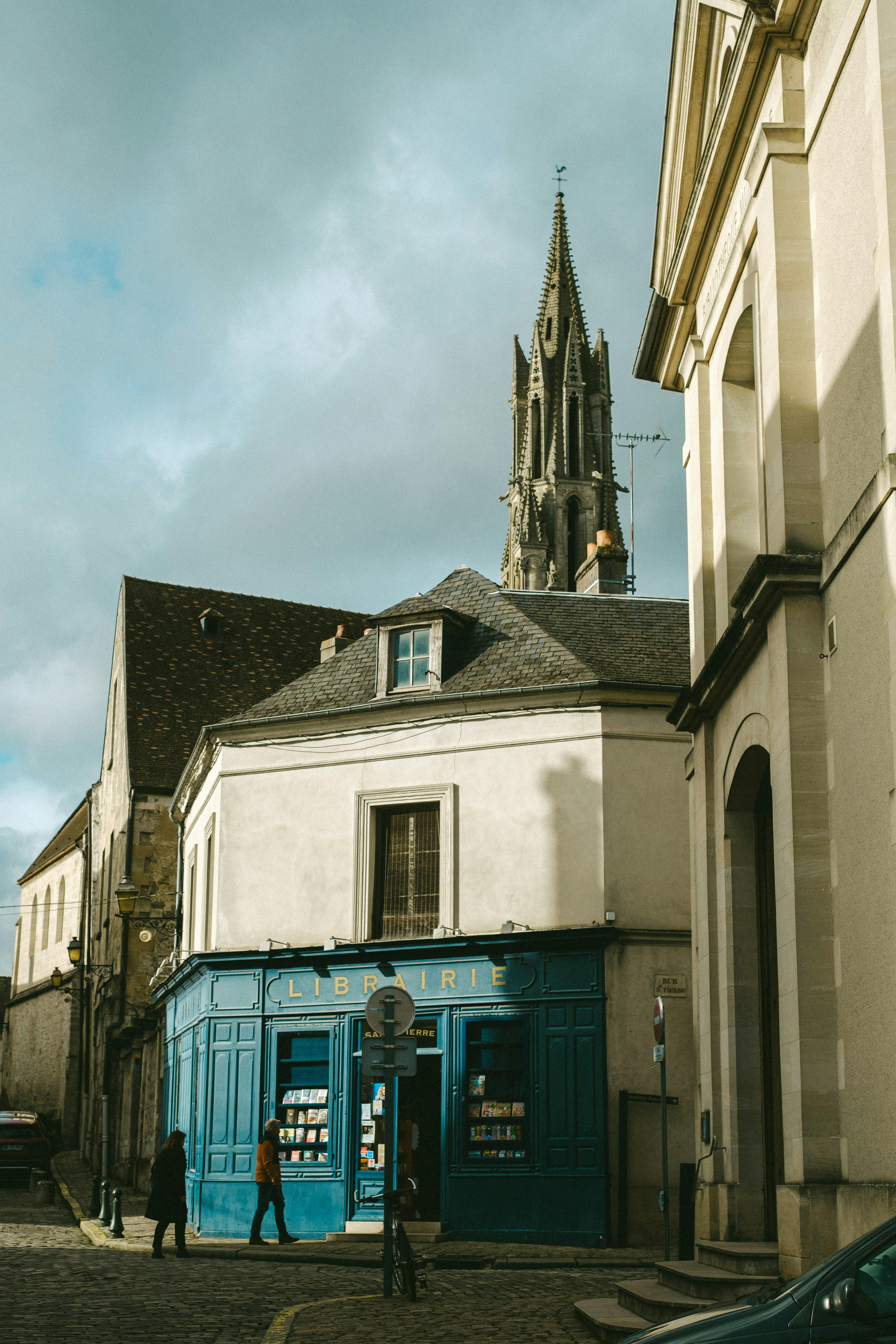 ingyenes Festői francia utca egy kék könyvesbolttal és a háttérben látható történelmi templomtoronnyal. Stockfotó