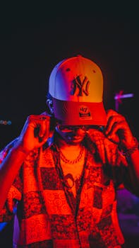 Vibrant urban portrait of a man adjusting his cap under colorful nightclub lights at night.