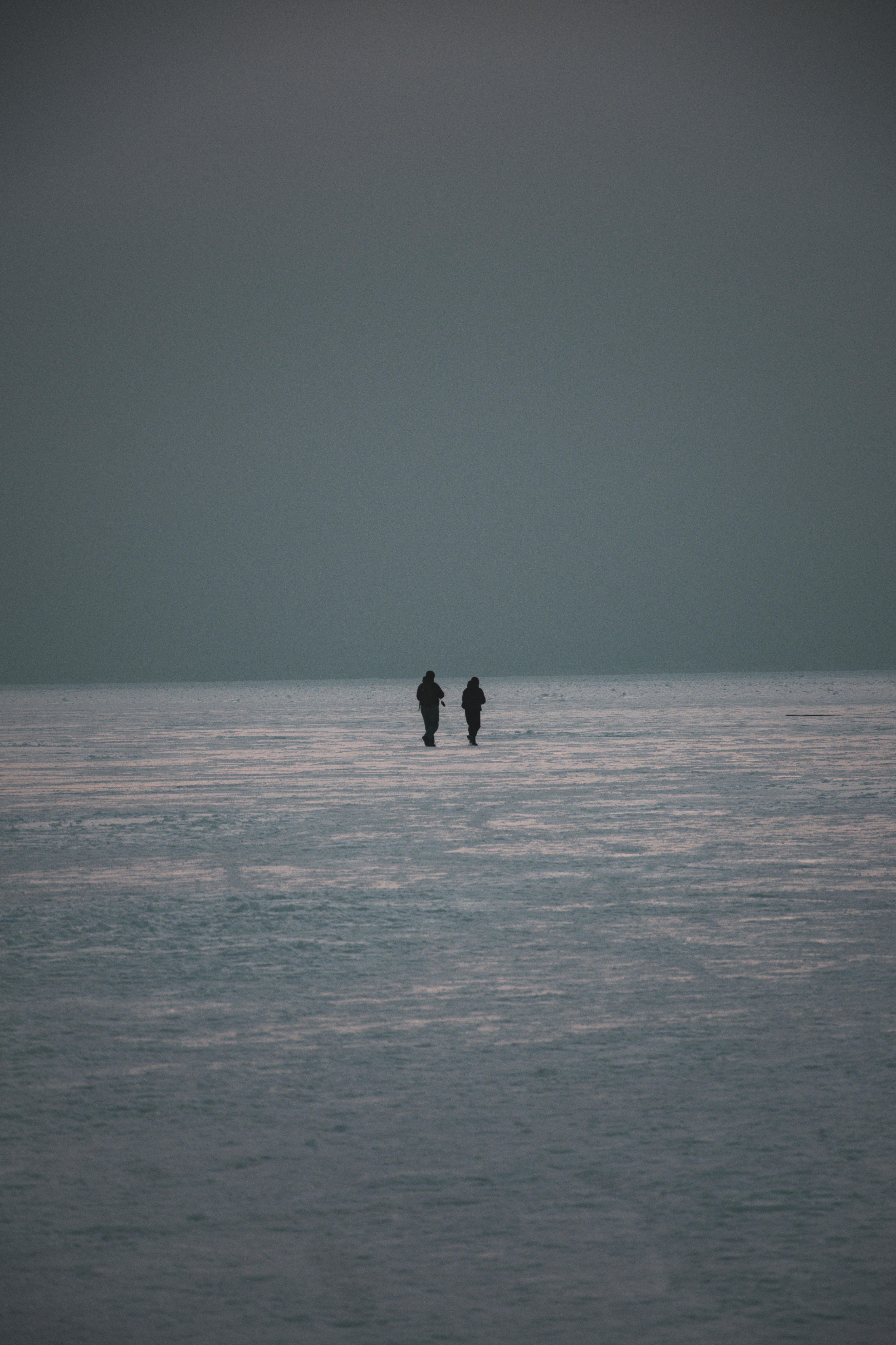 Δωρεάν Σιλουέτες δύο ανθρώπων που περπατούν σε μια απέραντη παγωμένη λίμνη στην Ουκρανία κατά τη διάρκεια του χειμώνα την αυγή. Φωτογραφία από στοκ φωτογραφιών