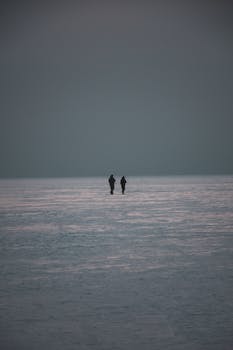 Silhouettes of two people walking across a vast frozen lake in Ukraine during winter at dawn.