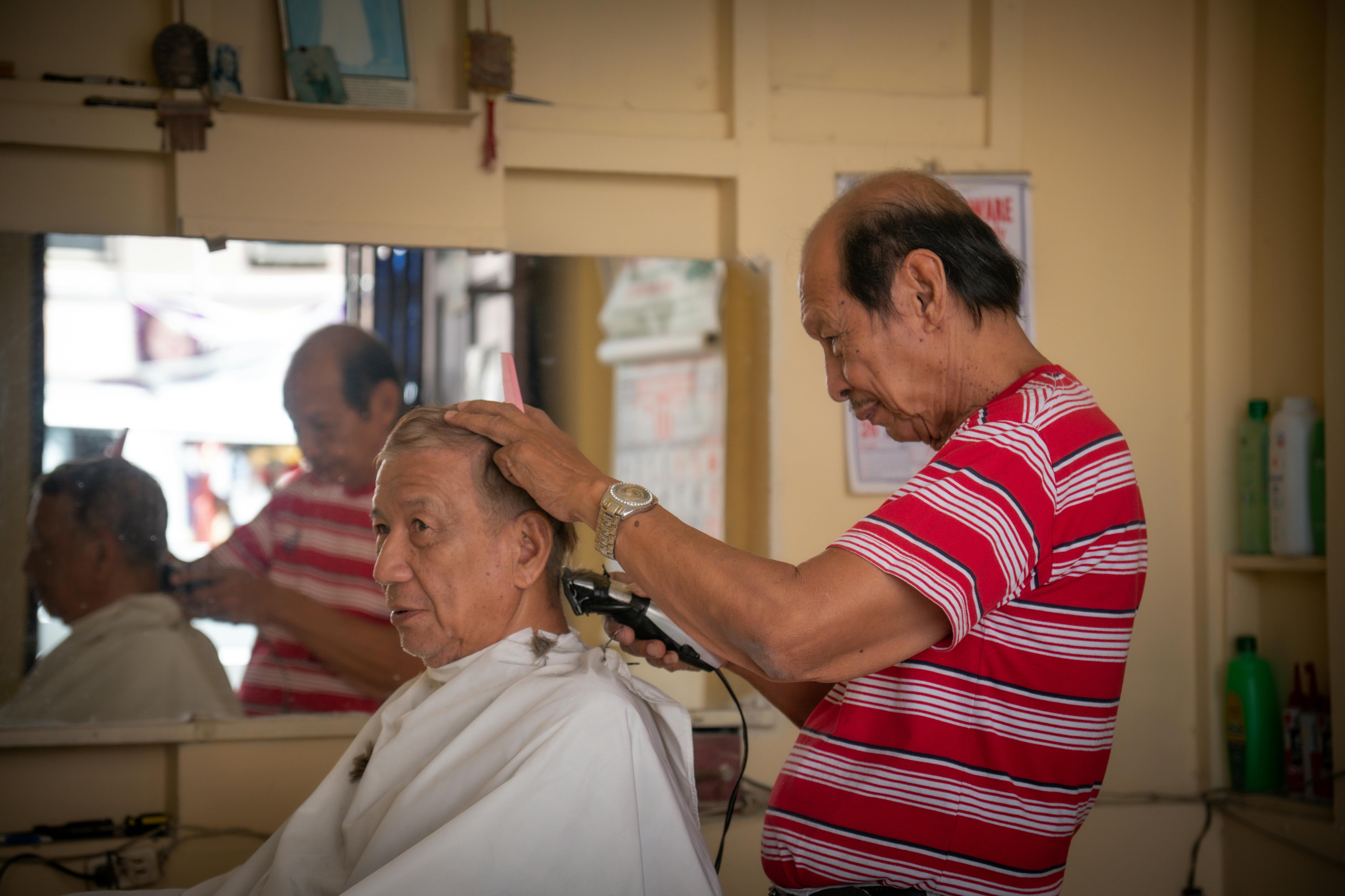 Gratis Un hombre mayor disfruta de un corte de pelo en un entorno de barbería clásica con un barbero experto. Foto de stock