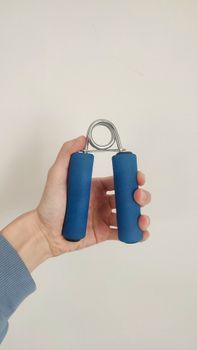 Close-up of a hand holding a blue grip strength exercise tool against a plain background.