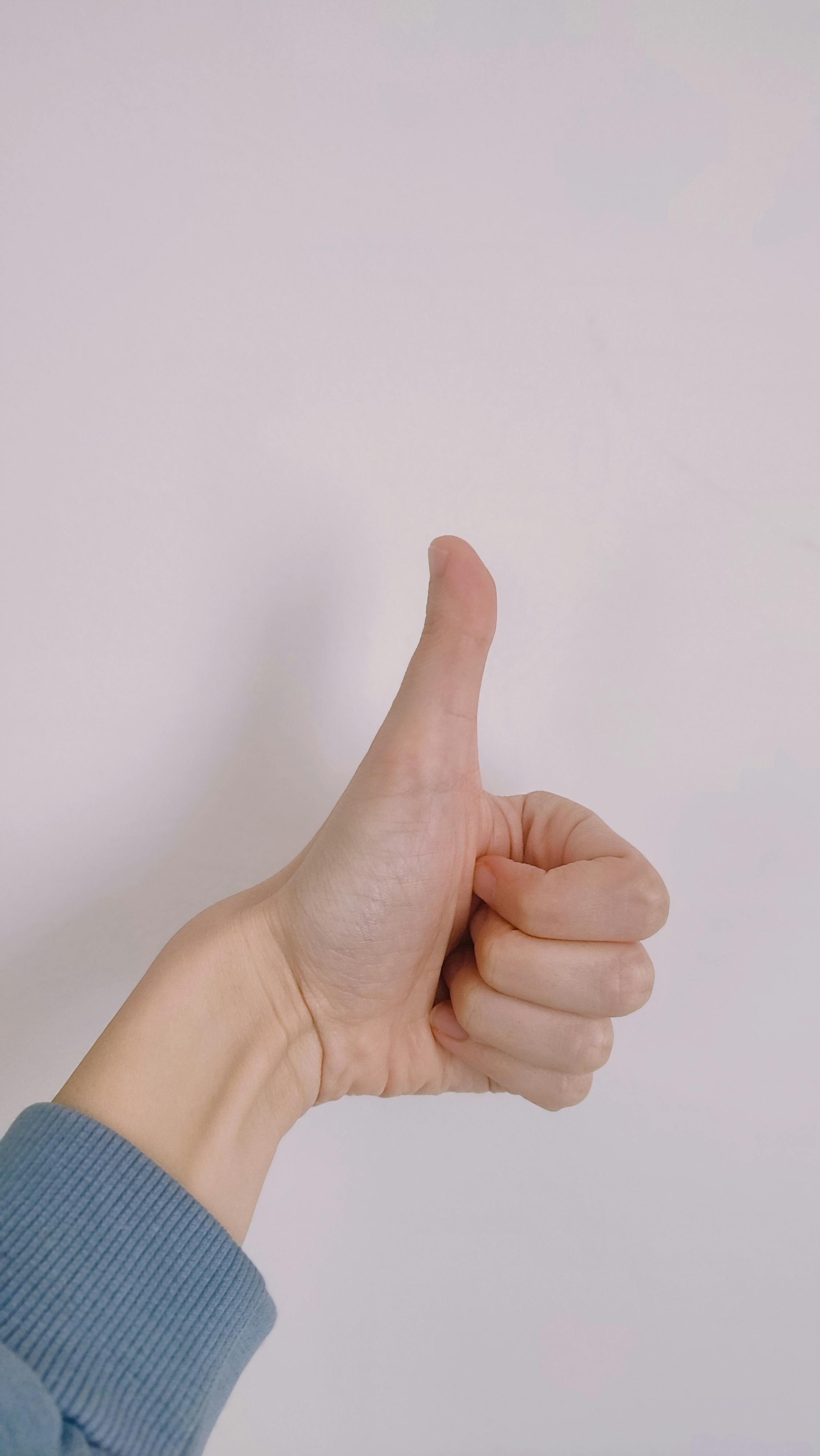 Free A close-up of a hand giving a thumbs-up sign against a simple background. Stock Photo