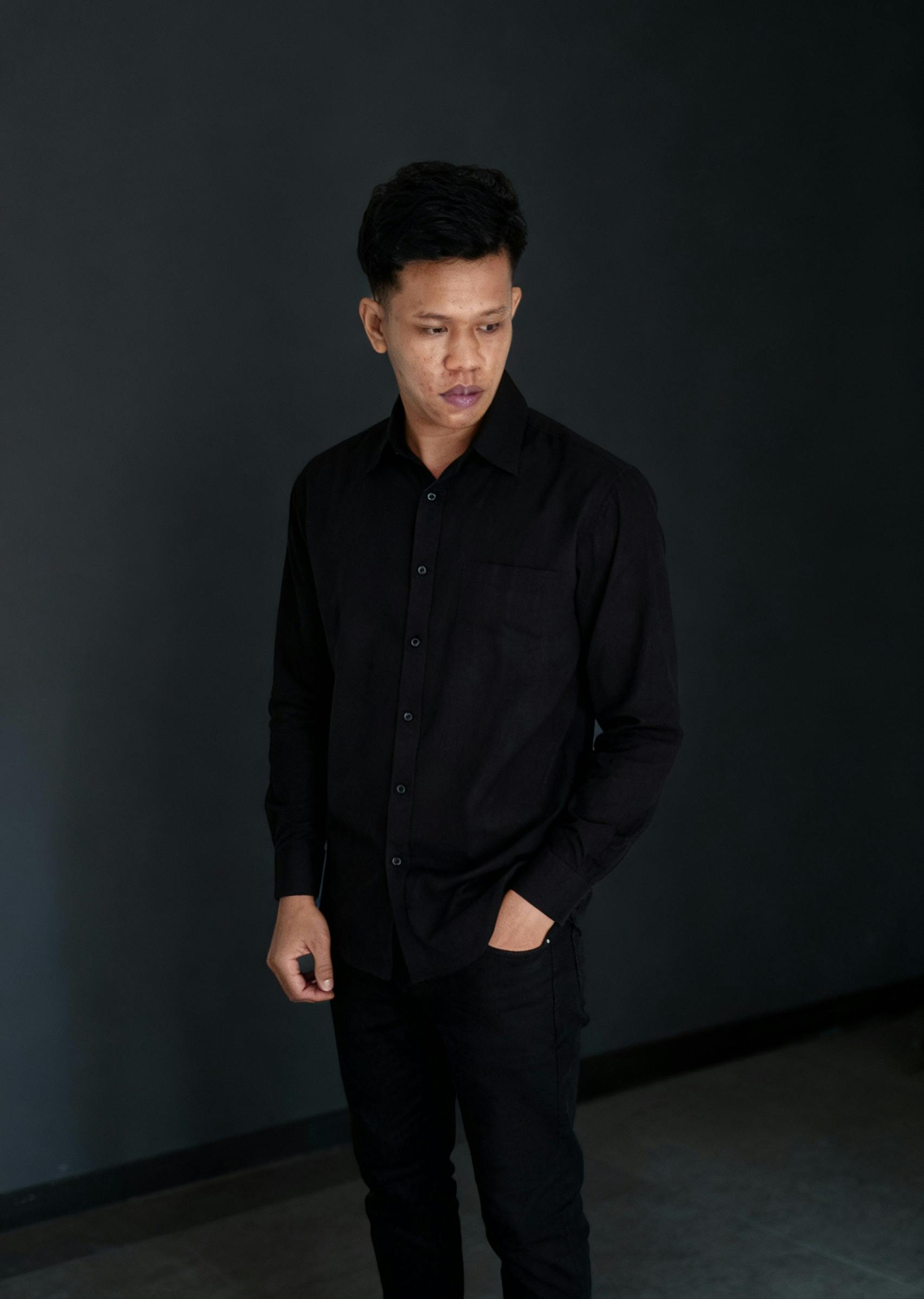 Gratis Ritratto di un giovane uomo vestito di nero, in piedi su uno sfondo scuro. Foto a disposizione