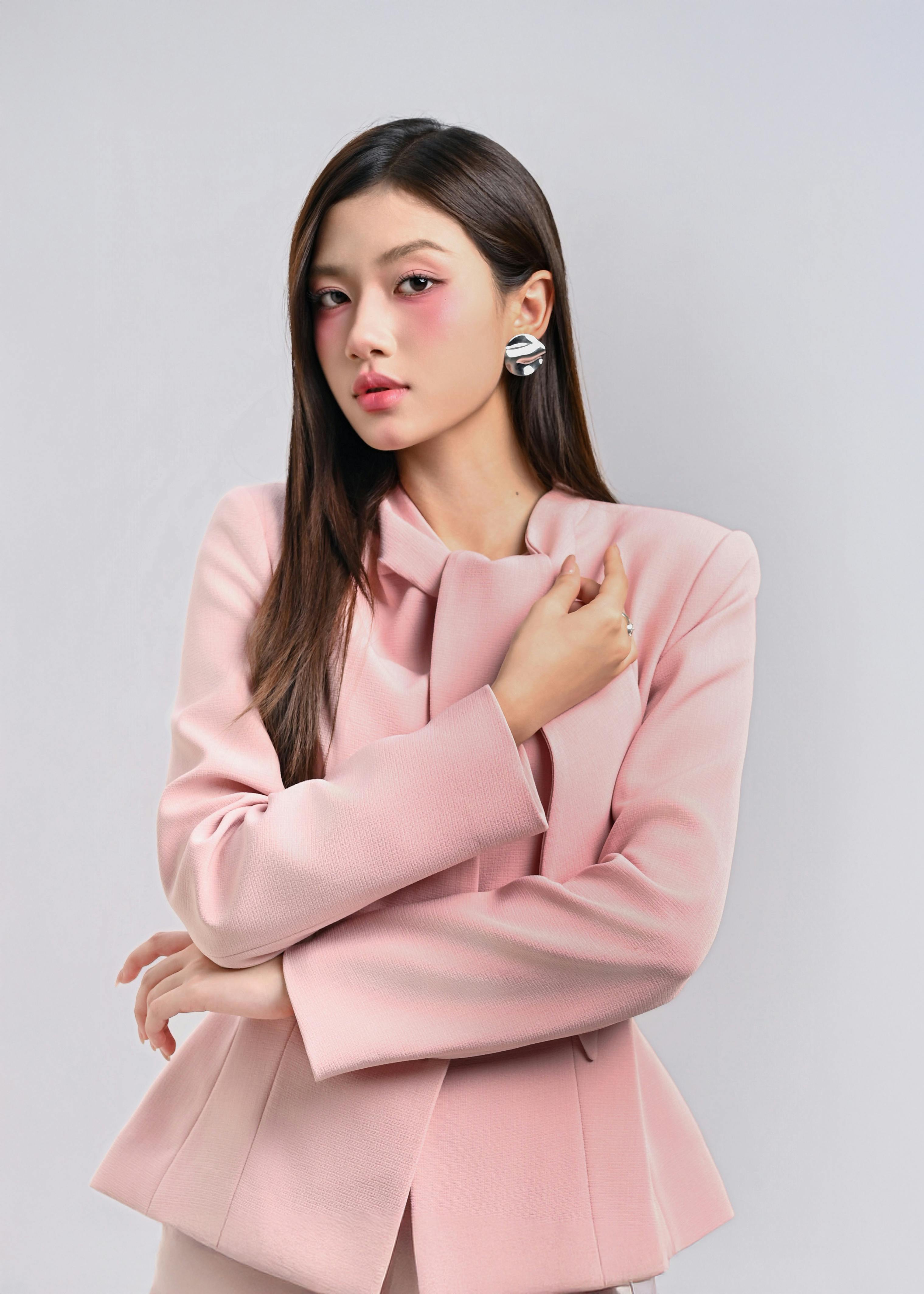 ฟรี หญิงสาวแต่งตัวมีสไตล์ในเสื้อเบลเซอร์สีชมพู โพสท่าอย่างมั่นใจโดยมีฉากหลังเป็นสีกลางๆ คลังภาพถ่าย