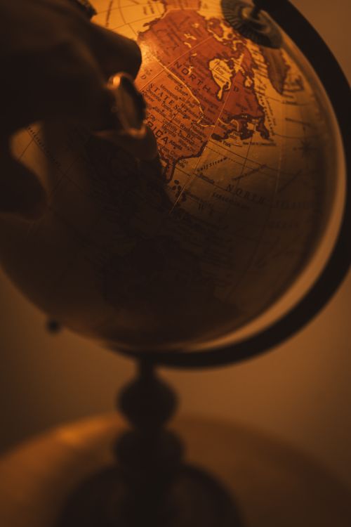 Free A vintage globe in warm tones with a hand pointing to a location. Stock Photo