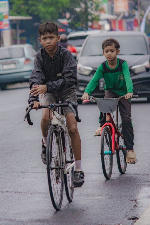 Free Two boys cycling on a wet street, showcasing urban lifestyle and road activity. Stock Photo